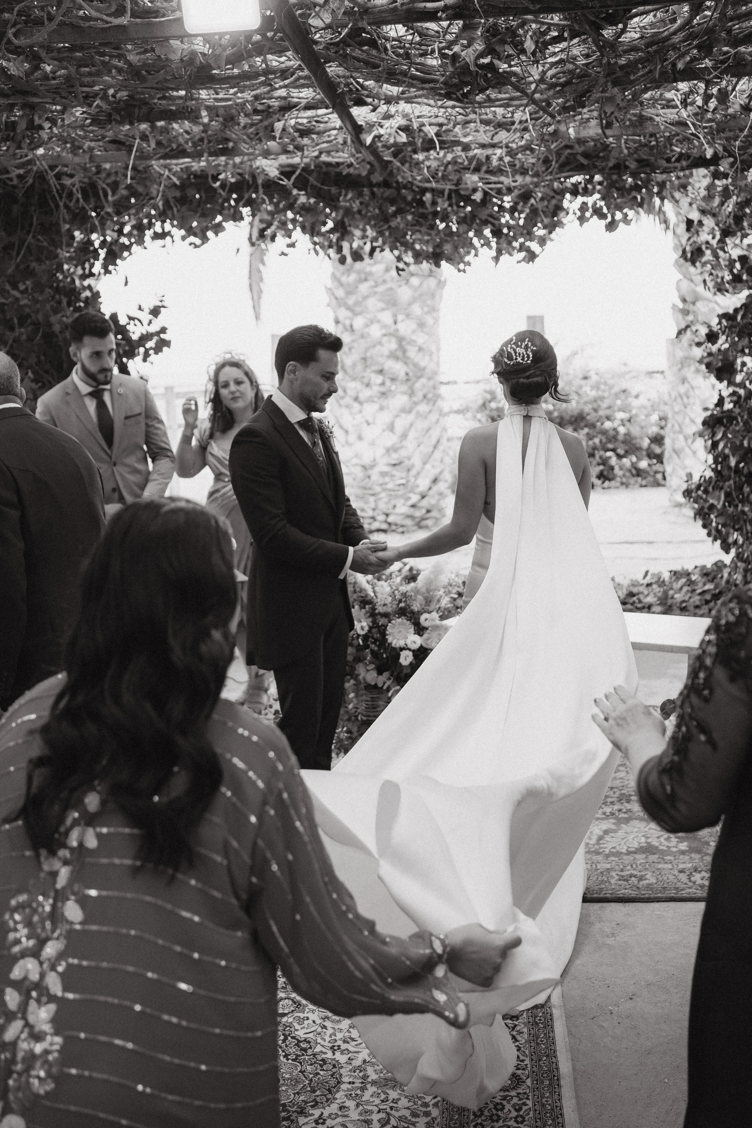 Una boda al aire libre con la pareja intercambiando votos y rodeada de invitados en un entorno natural.