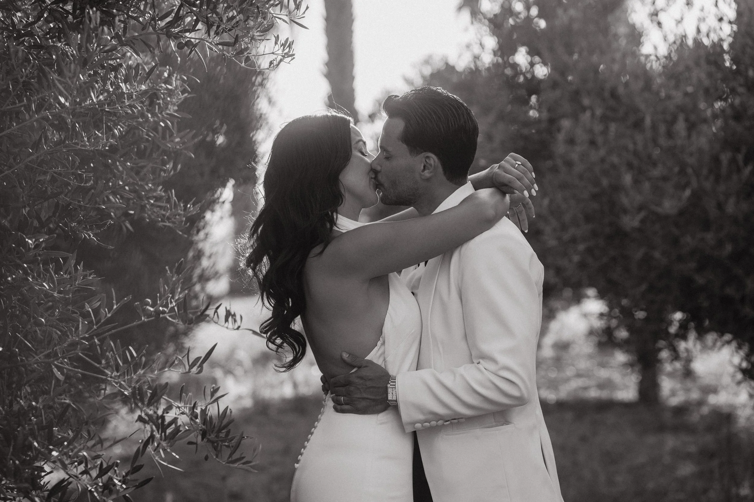 Pareja besándose al aire libre en un entorno natural, vestido formal, en un estilo romántico en blanco y negro.