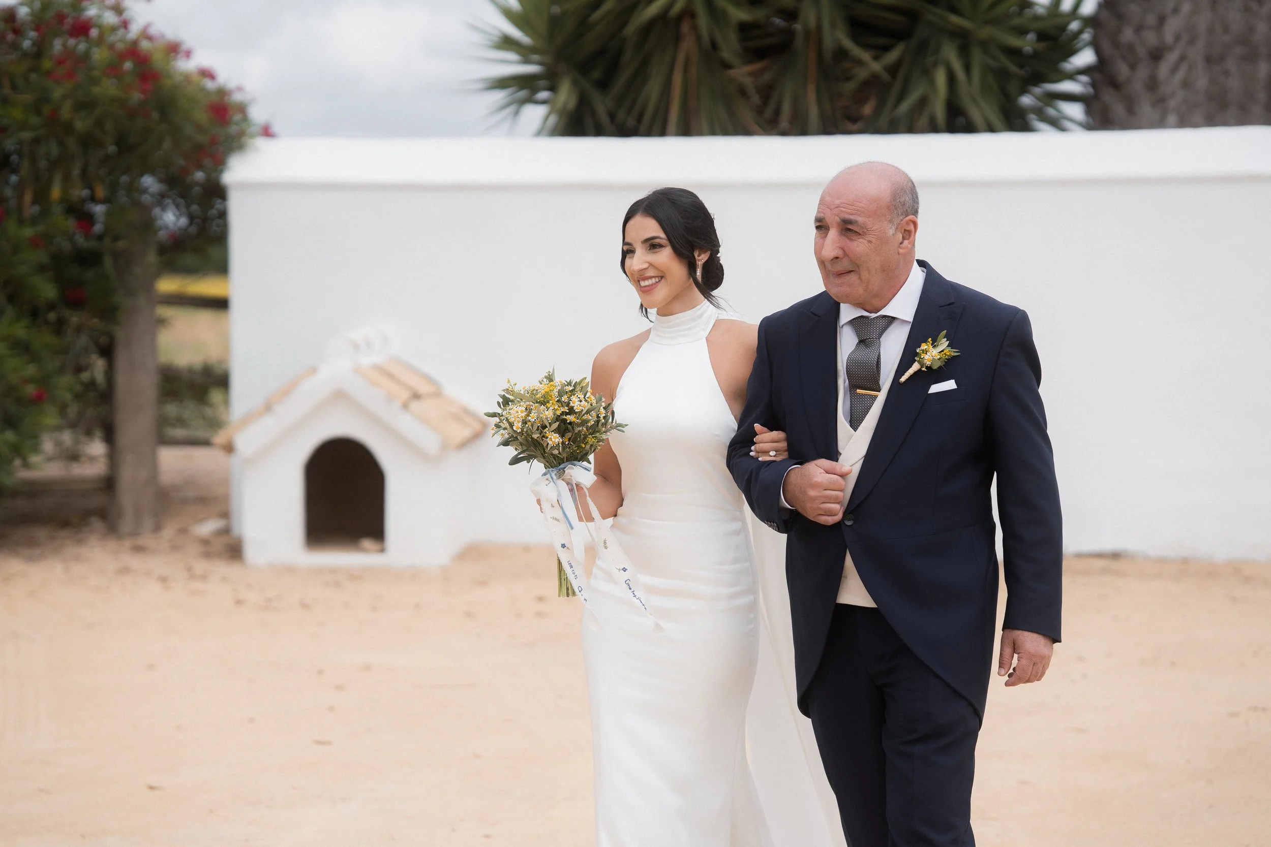 Mujer de vestido blanco y hombre de traje caminando de la mano en una boda en la hacienda Dehesa Bolaños en Jerez de la frontera, sonriendo.