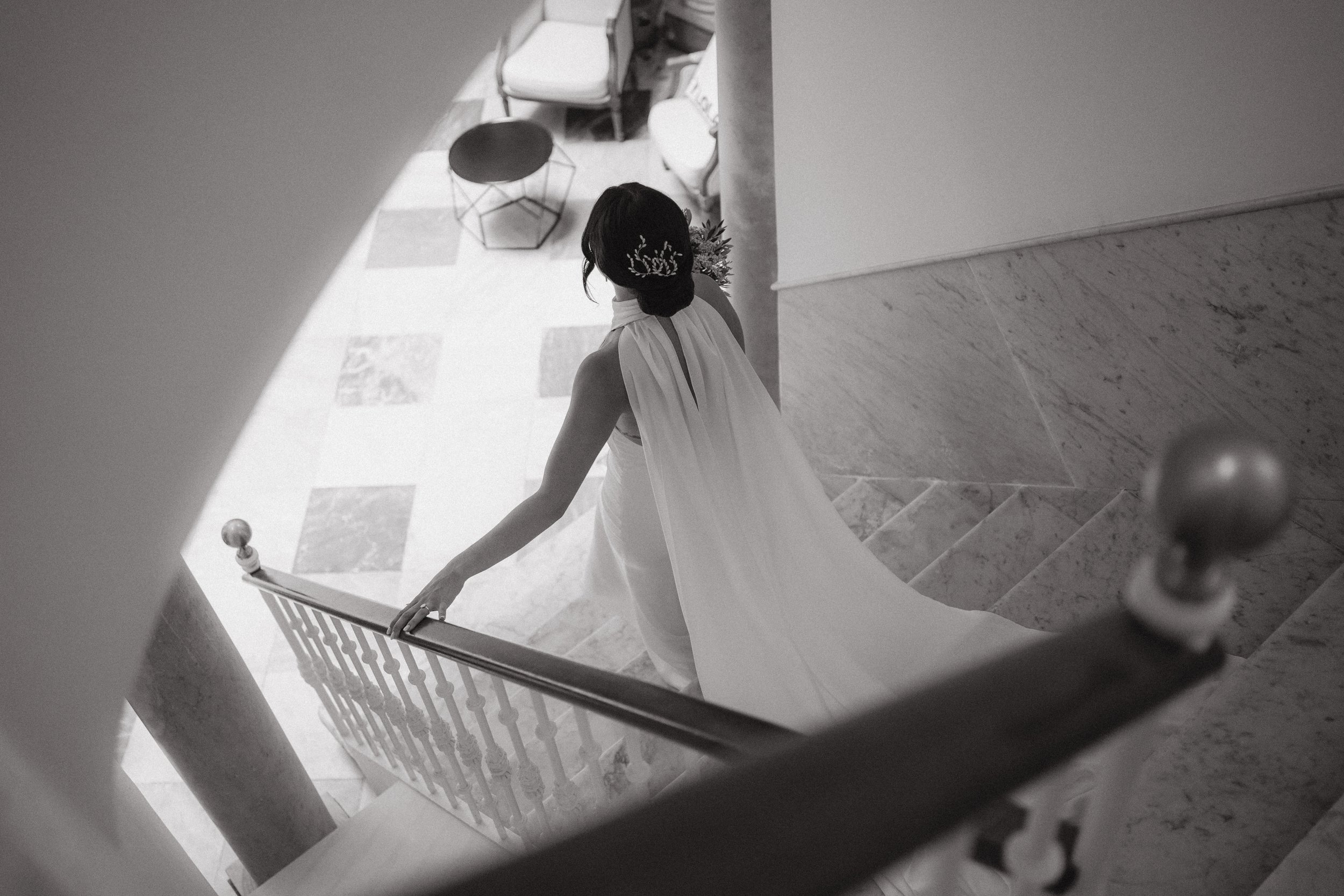 Una mujer en un vestido blanco caminando por unas escaleras de mármol, vista desde arriba.