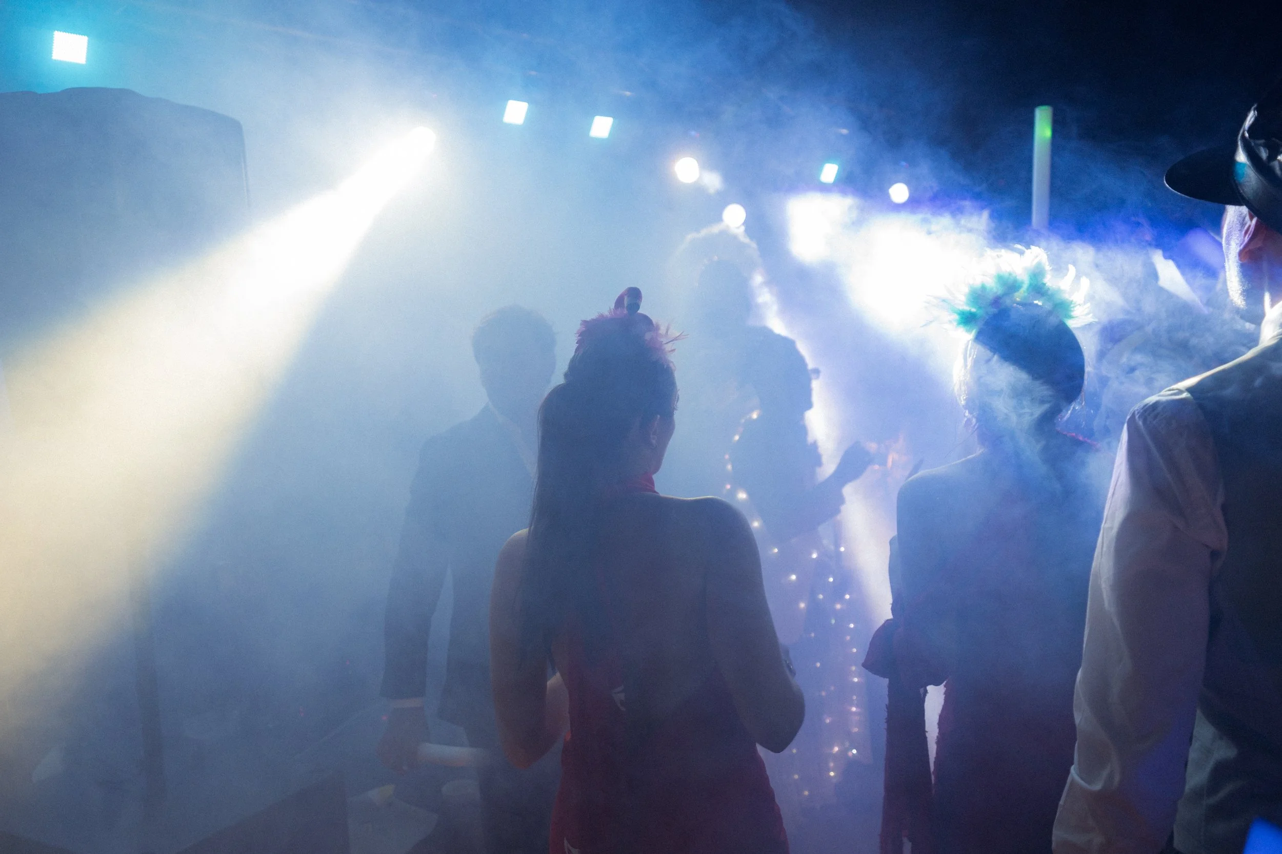 Personas bailando en una boda al aire libre con luces de colores y humo.