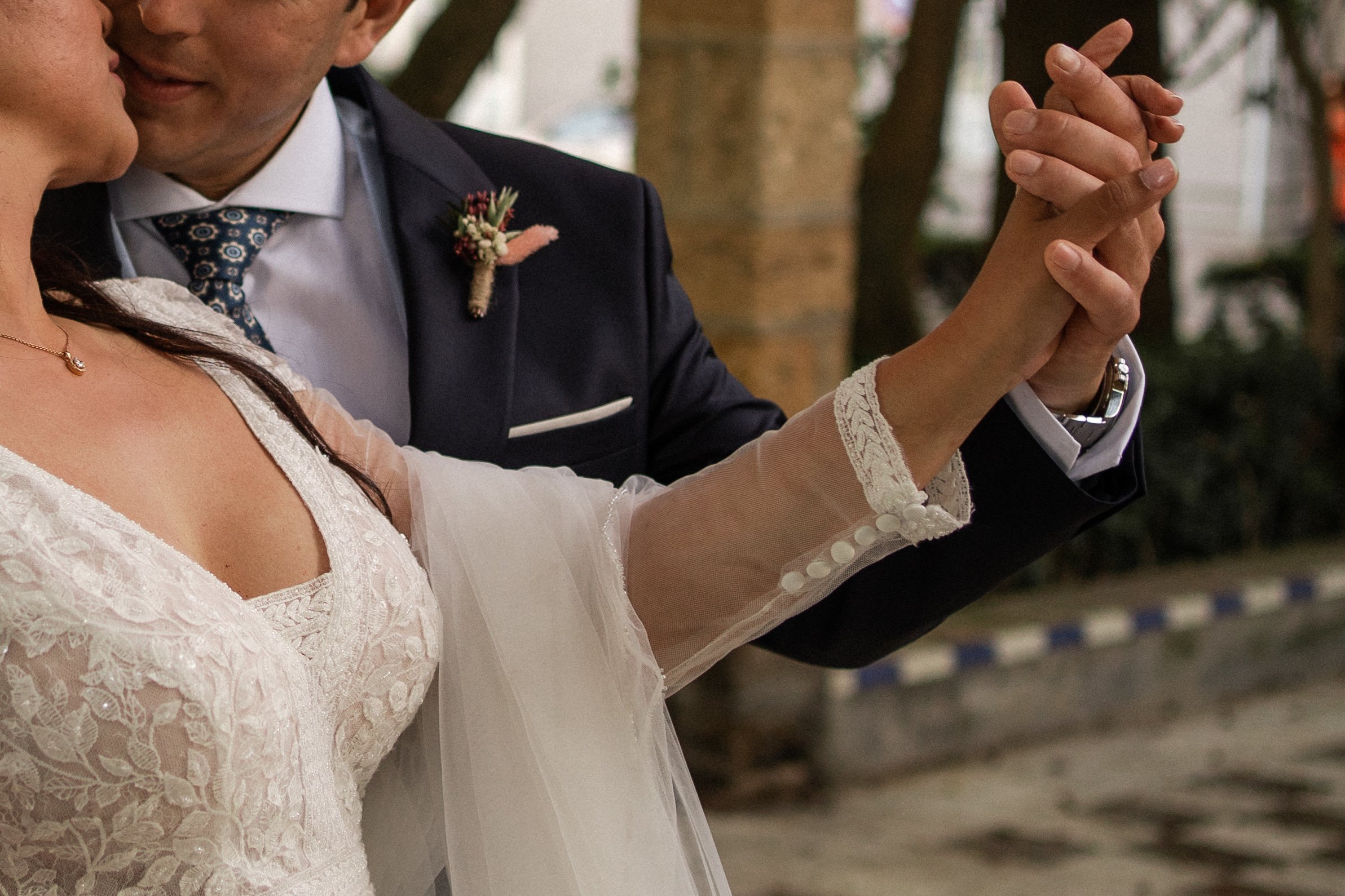 Pareja bailando en una boda, con enfoque en las manos unidas y el vestido de novia.