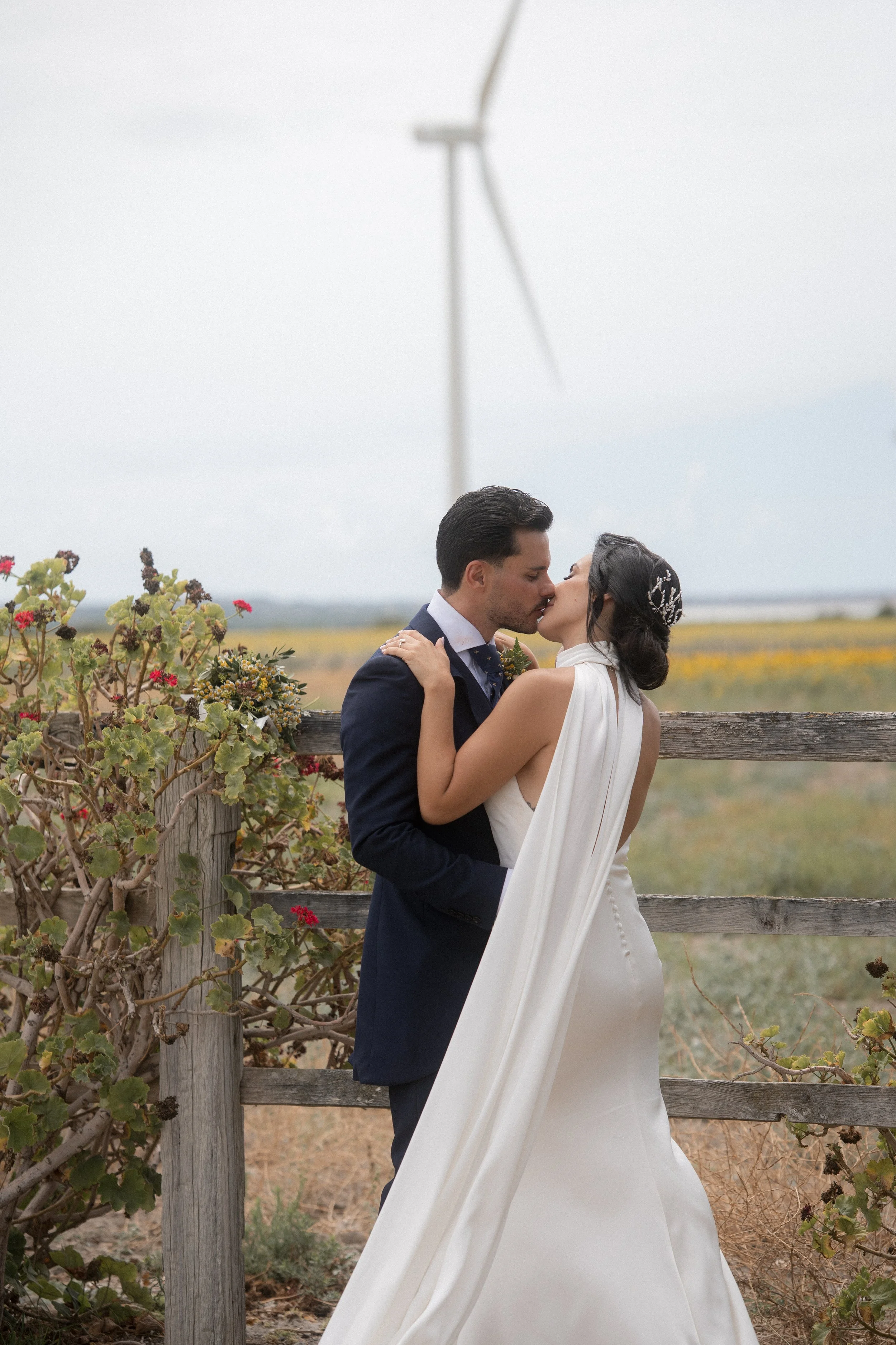Pareja de novios en un campo, besándose, con molino de viento en el fondo.