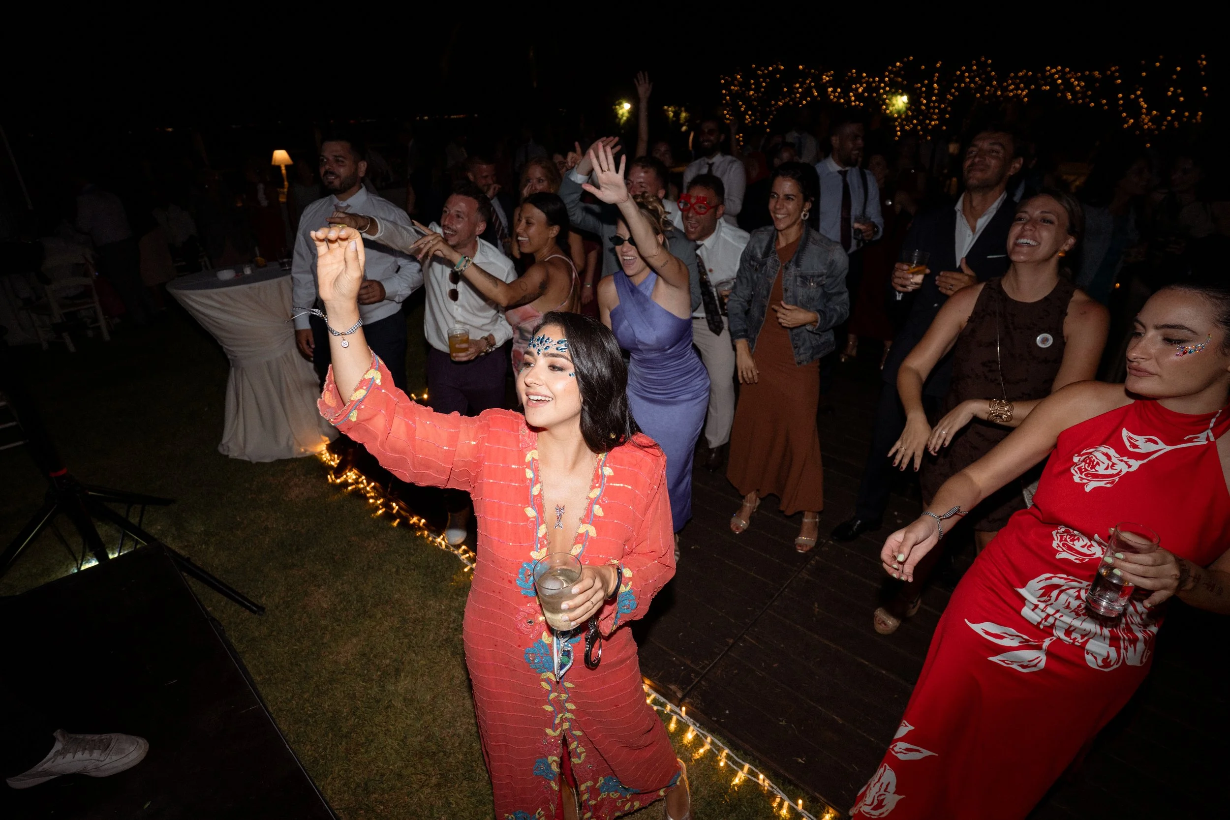 Grupo de personas bailando y disfrutando en una fiesta al aire libre en la noche, con decoraciones de luces.
