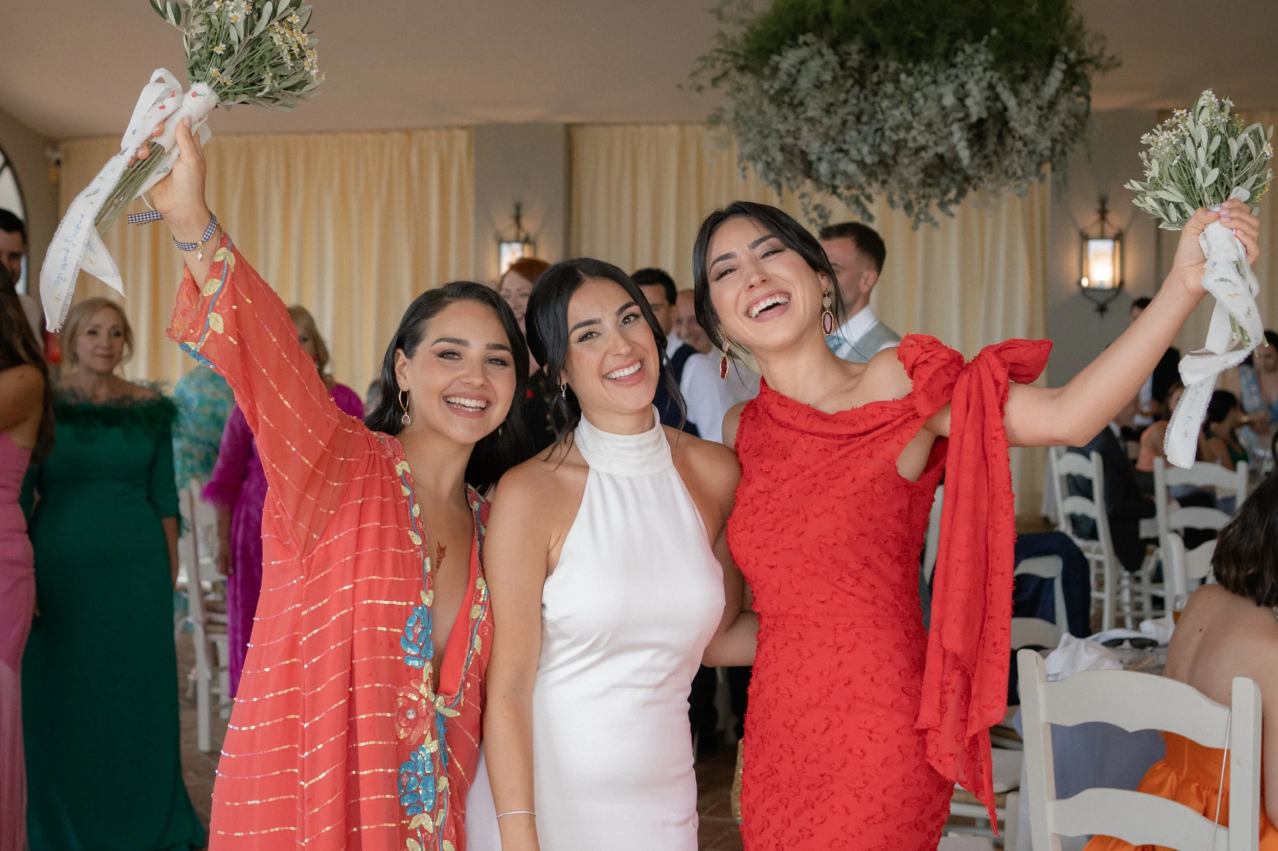 Tres mujeres en vestidos elegantes sonriendo y sosteniendo bouquets en una celebración
