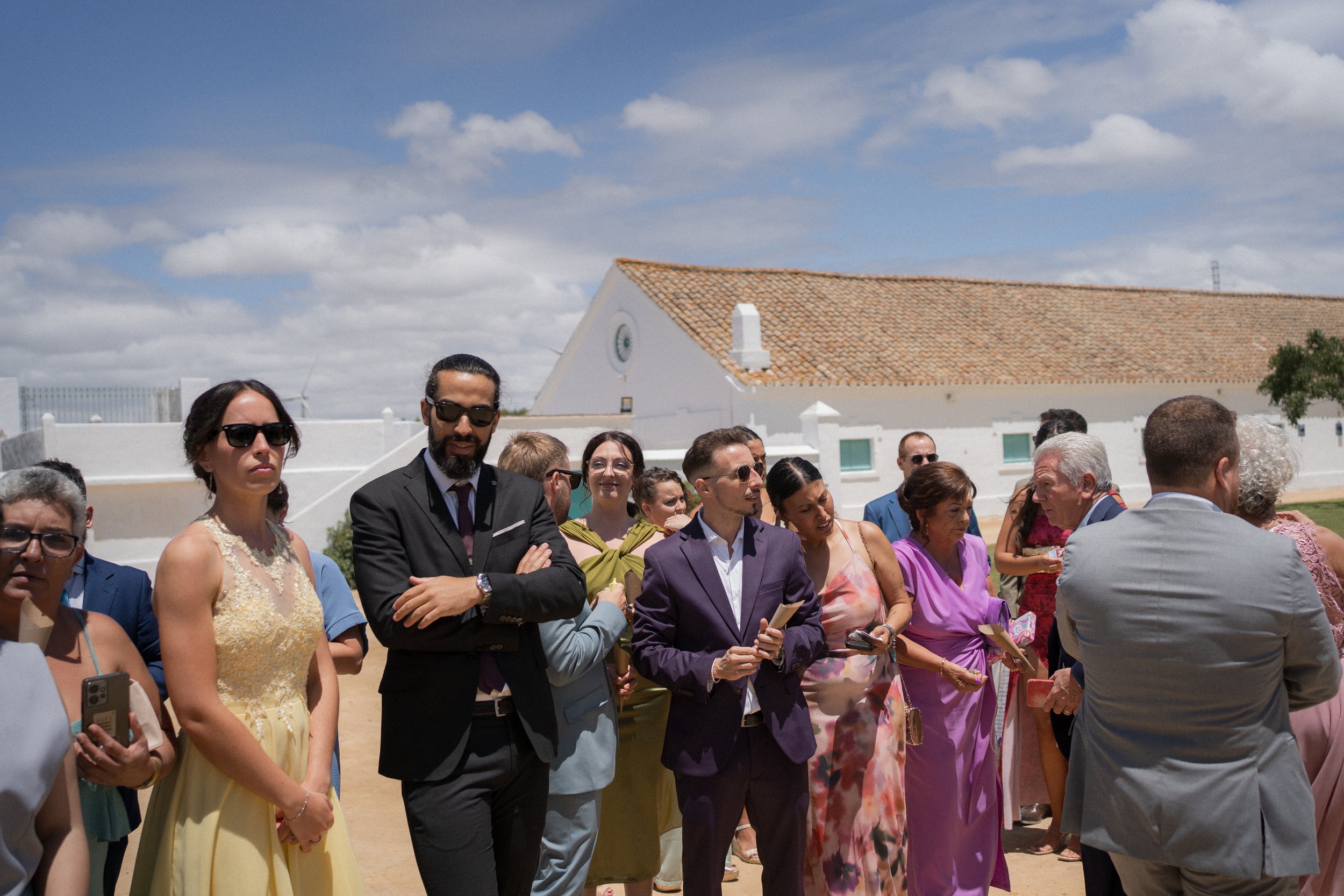 Grupo de personas en una ceremonia al aire libre, con una iglesia blanca de fondo y cielo nublado.
