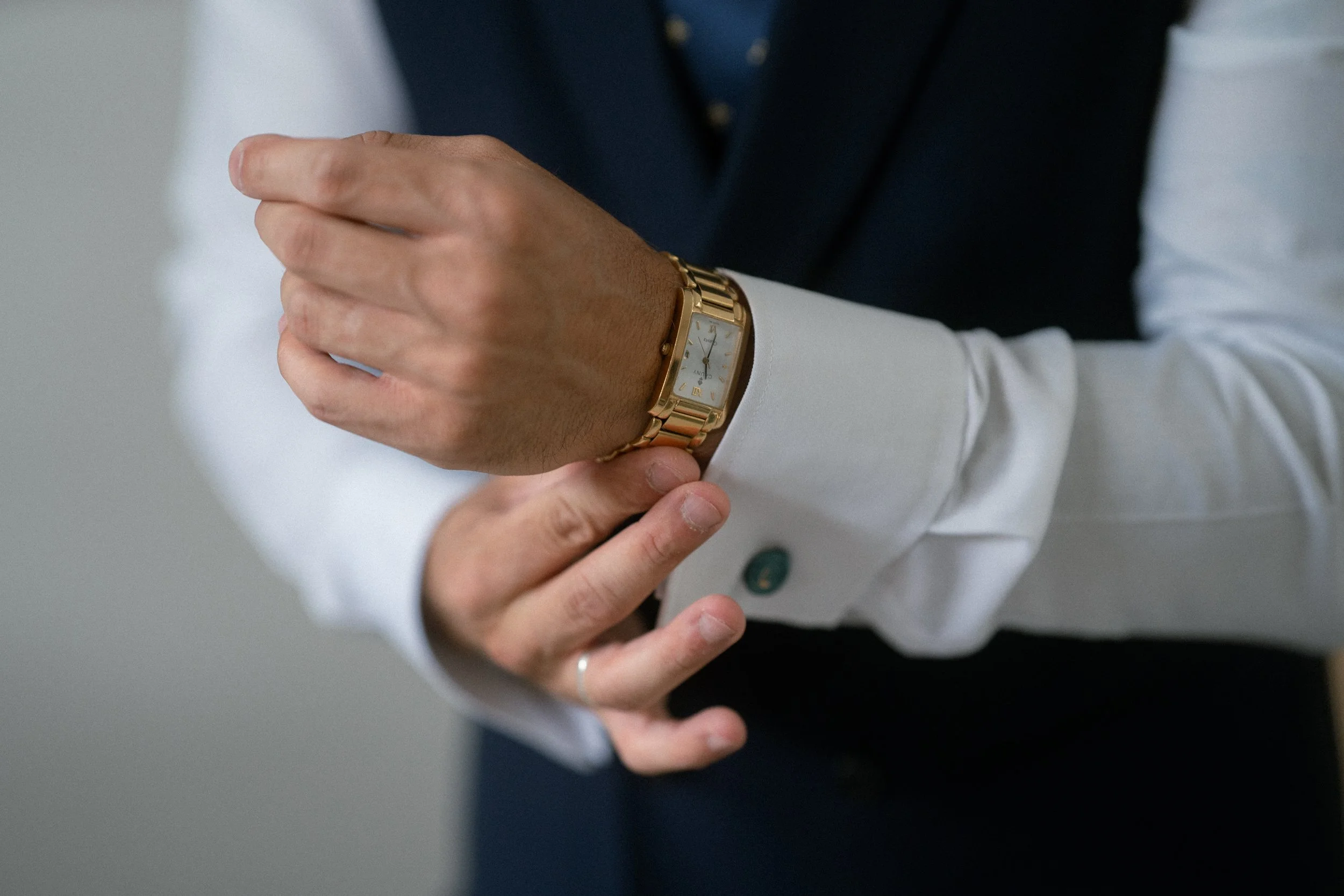 Persona ajustándose la manga de su camisa para poner un reloj dorado en la muñeca.