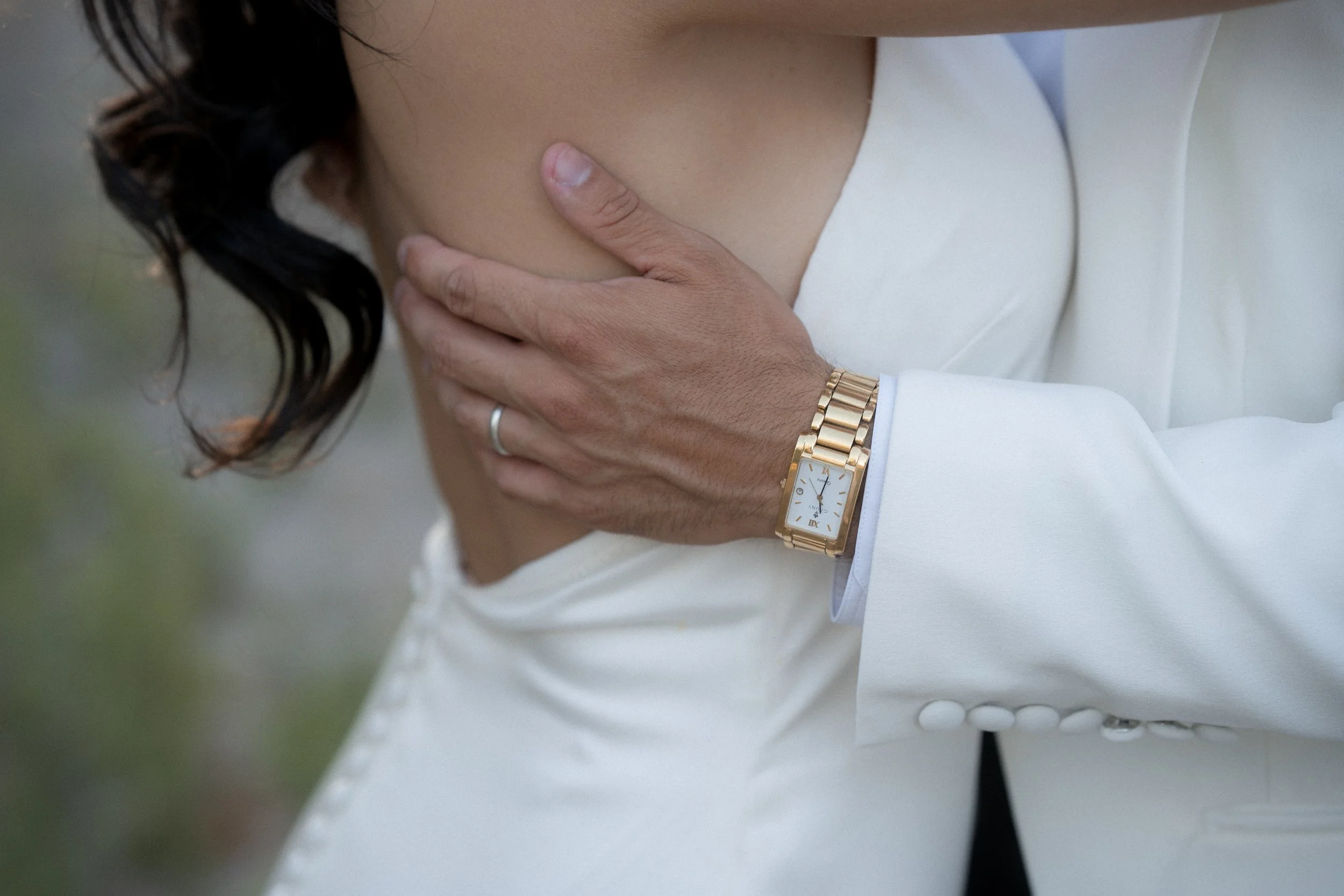 persona con vestido blanco y reloj dorado tocándose el hombro izquierdo
