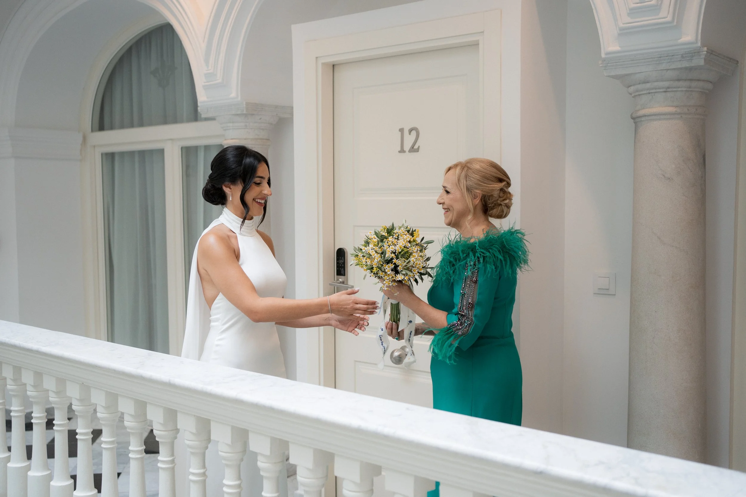 Mujer con vestido de novia entregando ramo a mujer mayor en pasillo elegante