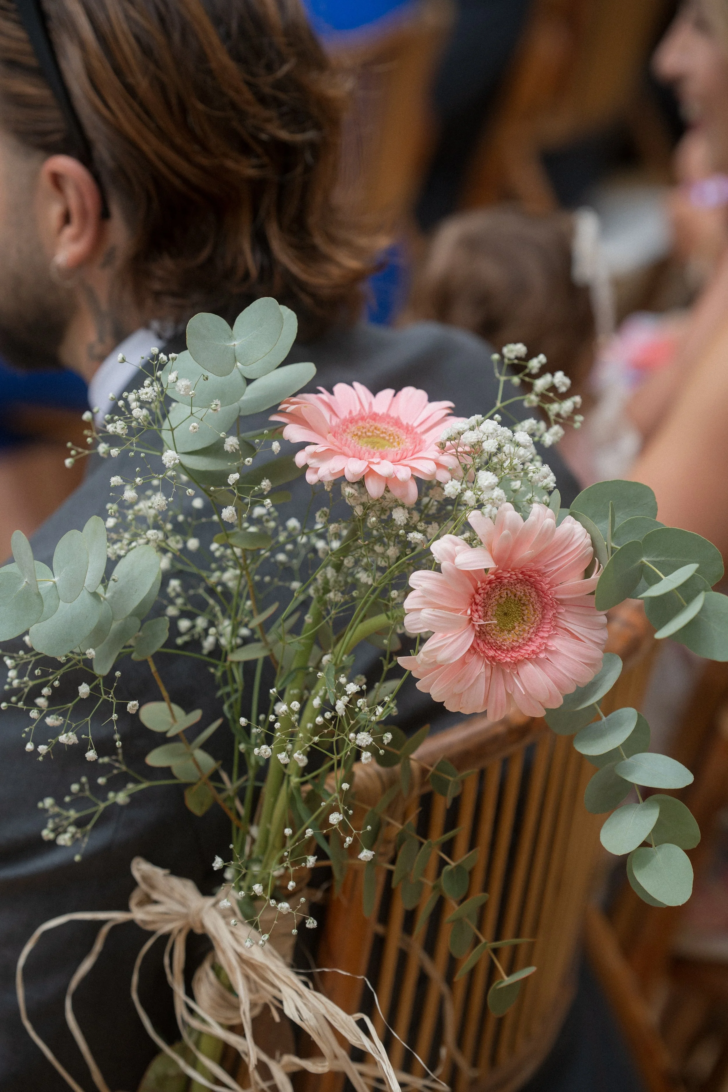 Ramo de flores con gerberas rosas, eucalipto y pequeñas flores blancas sobre la espalda de una persona en un evento.