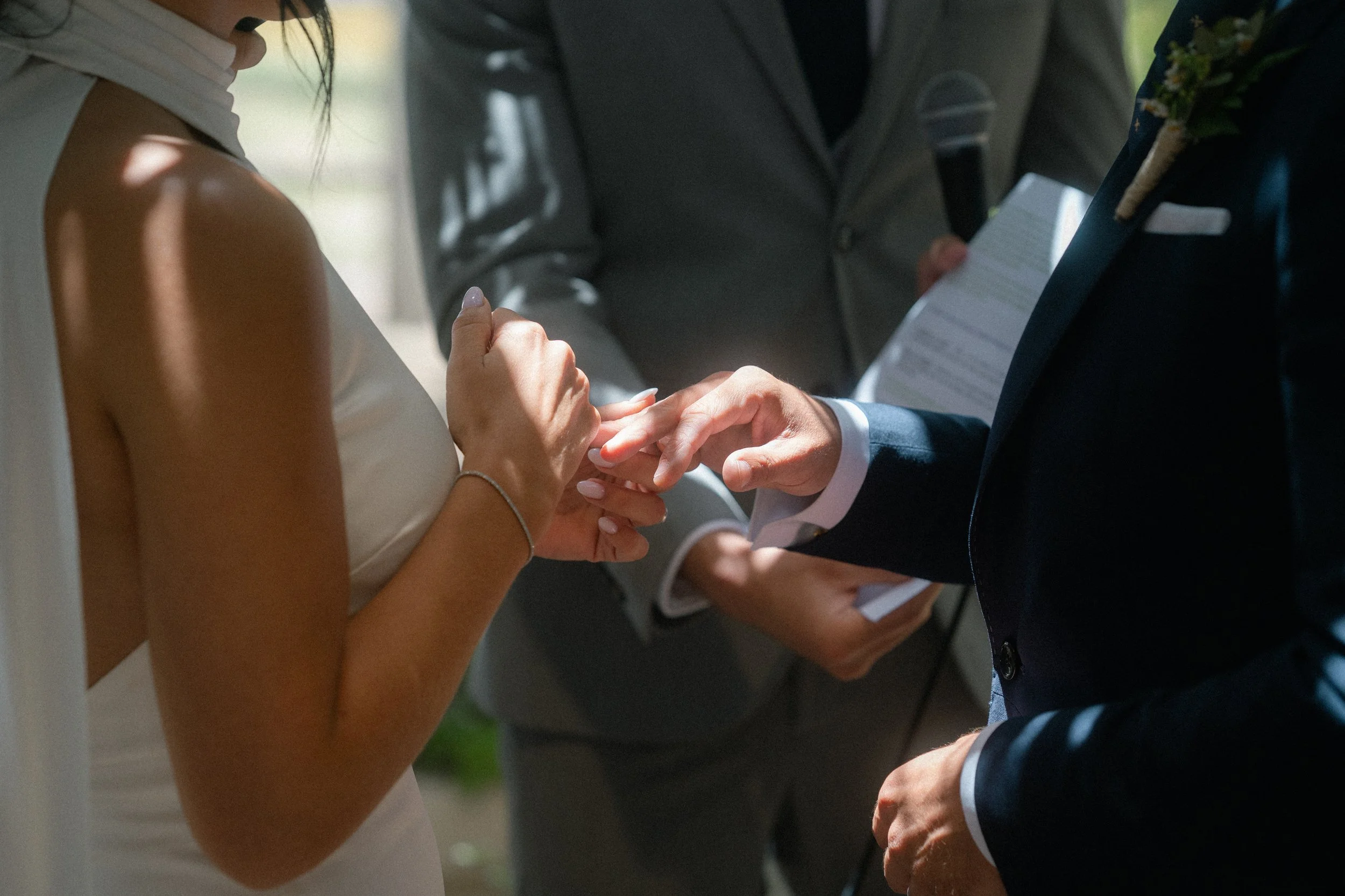 Una pareja intercambiando anillos durante su boda, con un oficiante en el fondo y un micrófono en su mano.