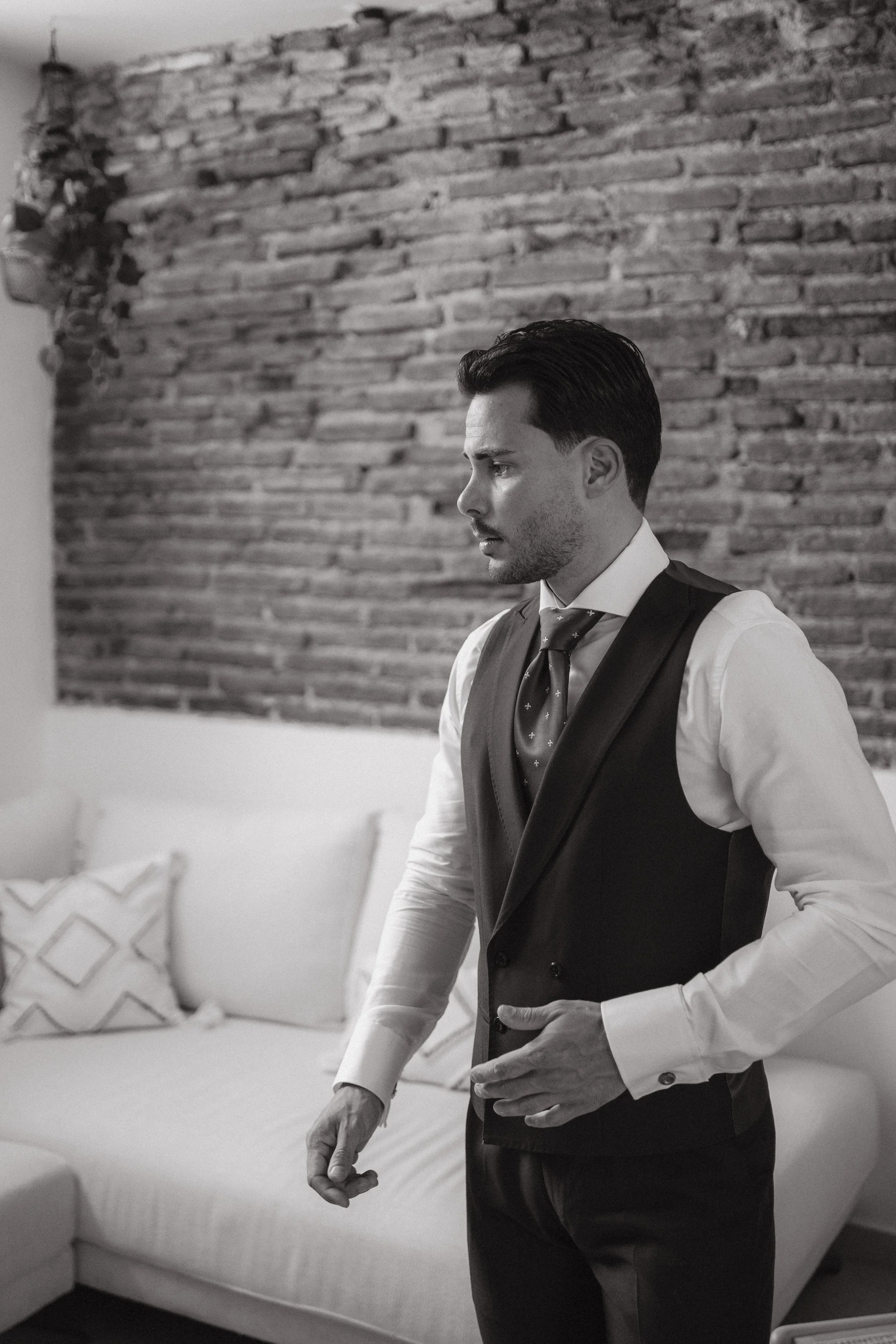Joven vestido con traje formal en un ambiente interior con pared de ladrillos y sillón con cojines