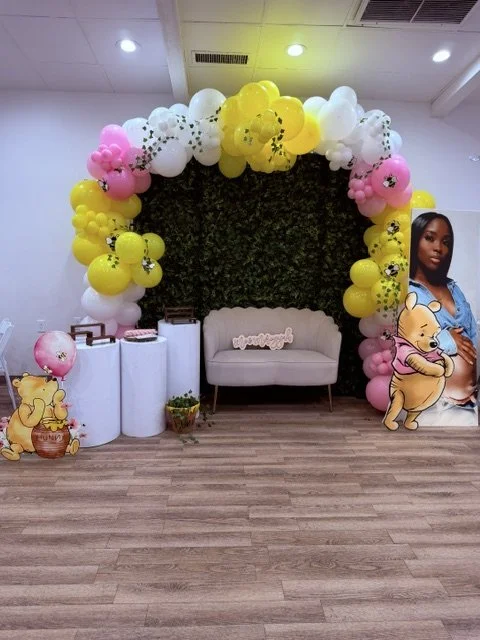 Winnie the Pooh baby shower rentals in Philadelphia featuring a greenery wall, balloon arch, white pedestals, and luxury velvet loveseat