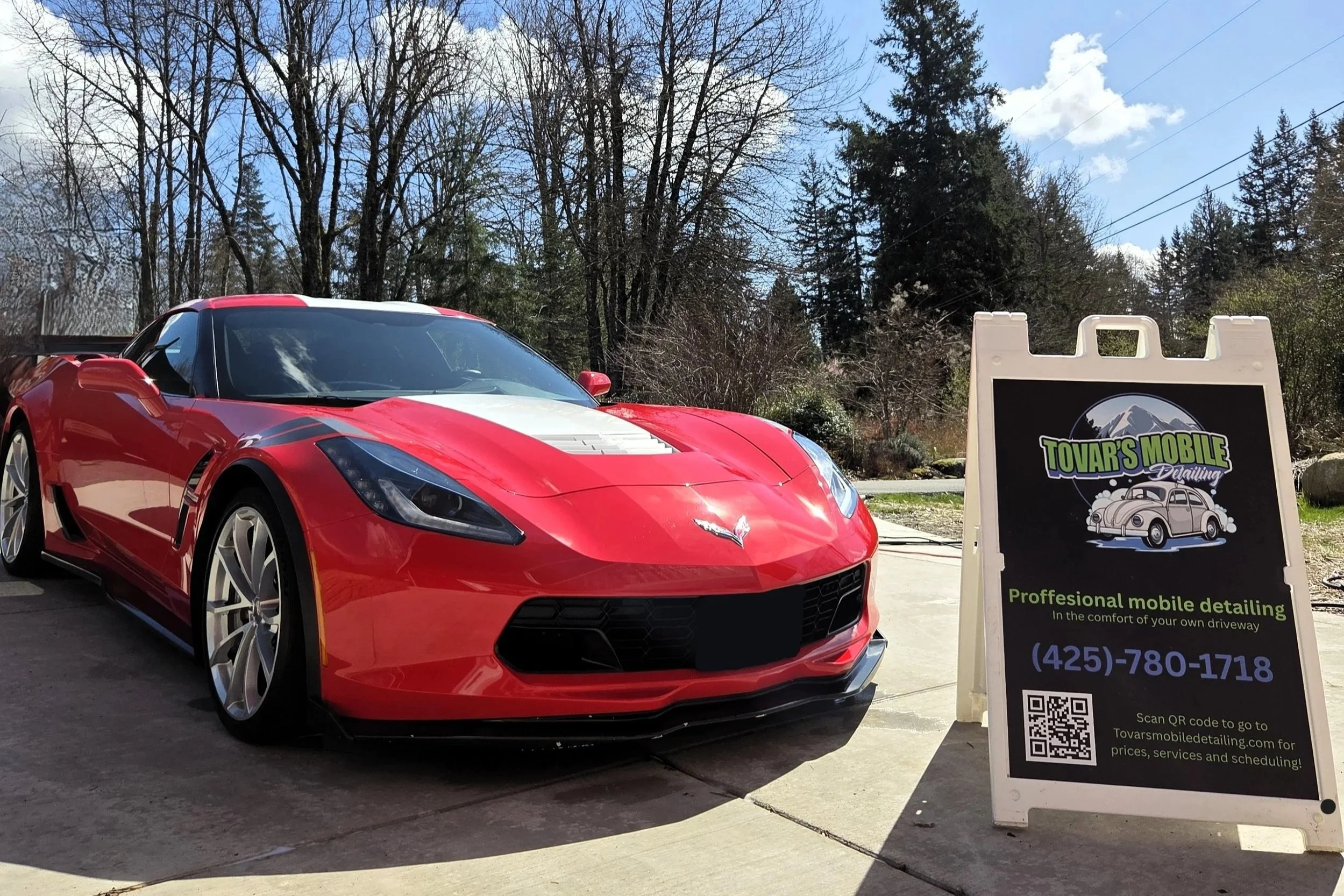 Red Chevrolet Corvette car parked on driveway next to a black sign with green and purple text for Tovar's Mobile Detailing, offering professional mobile detailing services.