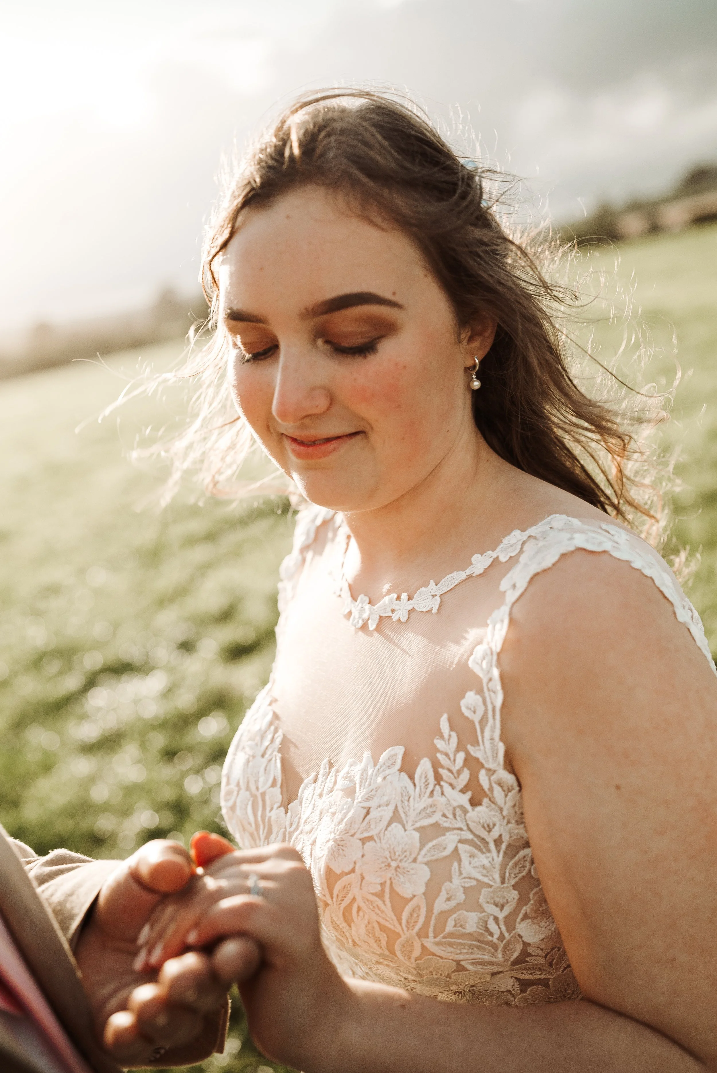 Bride in lace wedding dress smiling, holding hands in a field.
