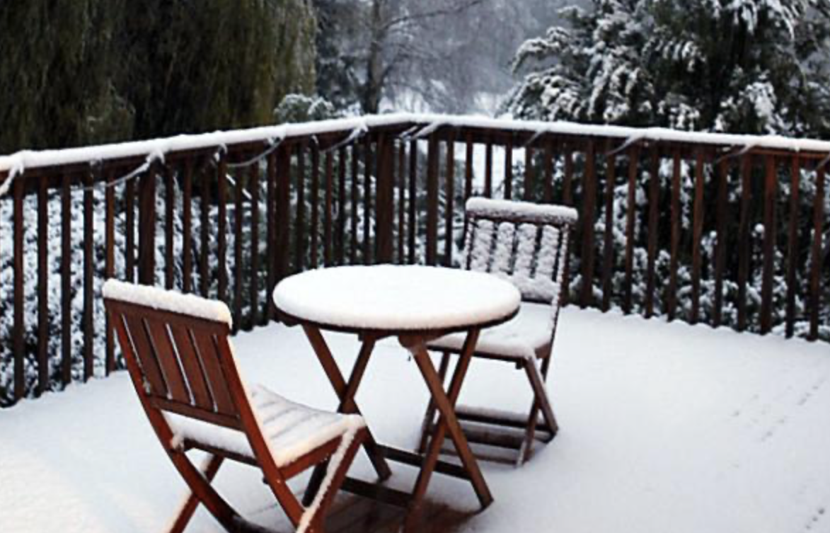 Snow covered table and chairs on a snow covered deck.