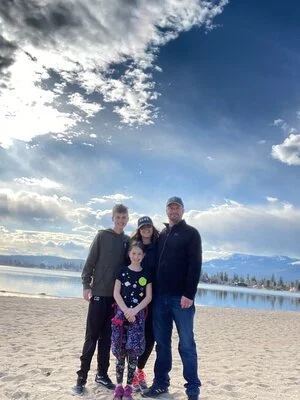 A professional outdoor family portrait on a sandy beach with mountains in the background.
