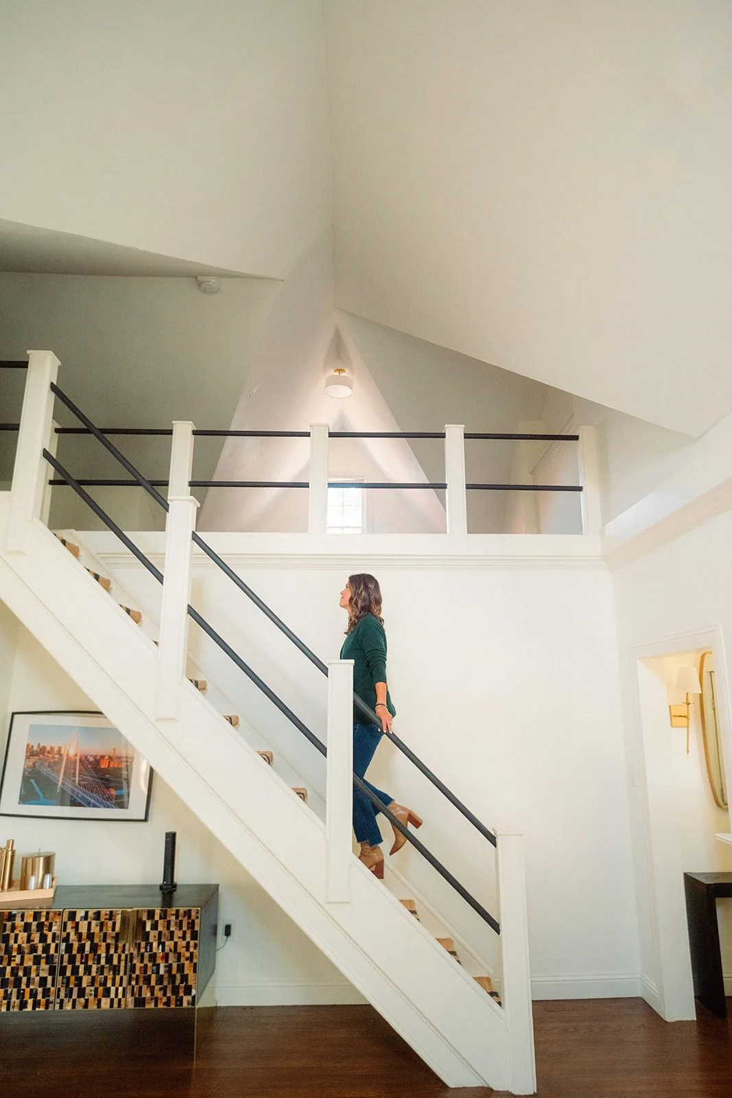Janel Gion walking up a staircase inside a well-lit modern home with white walls and a high ceiling.