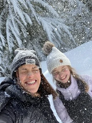 A professional photo of a mother and daughter smiling together in a snowy forest, representing a winter photo session.