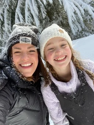 A close-up selfie of a woman and a girl smiling in a snowy forest, illustrating tips on taking a good selfie.