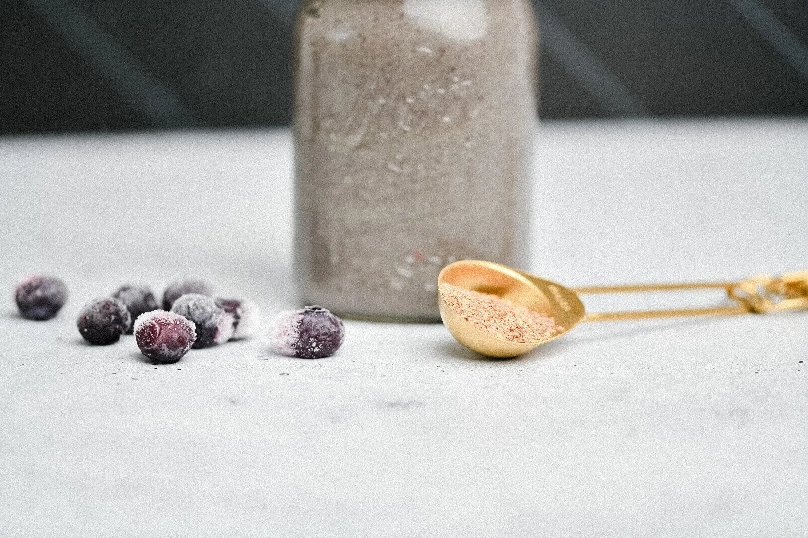 A superfood smoothie in a mason jar with a scoop of a superfood mix and frozen blueberries.