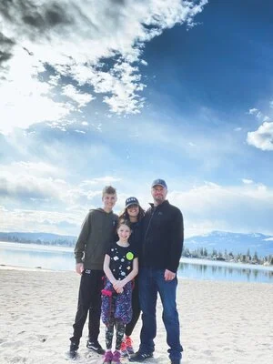 A professional family portrait on a beach with a scenic view of the water and mountains.