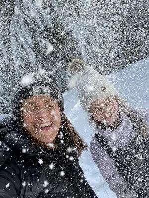 A close-up selfie of a woman and a girl smiling and laughing while it is snowing, illustrating tips on taking a good selfie.