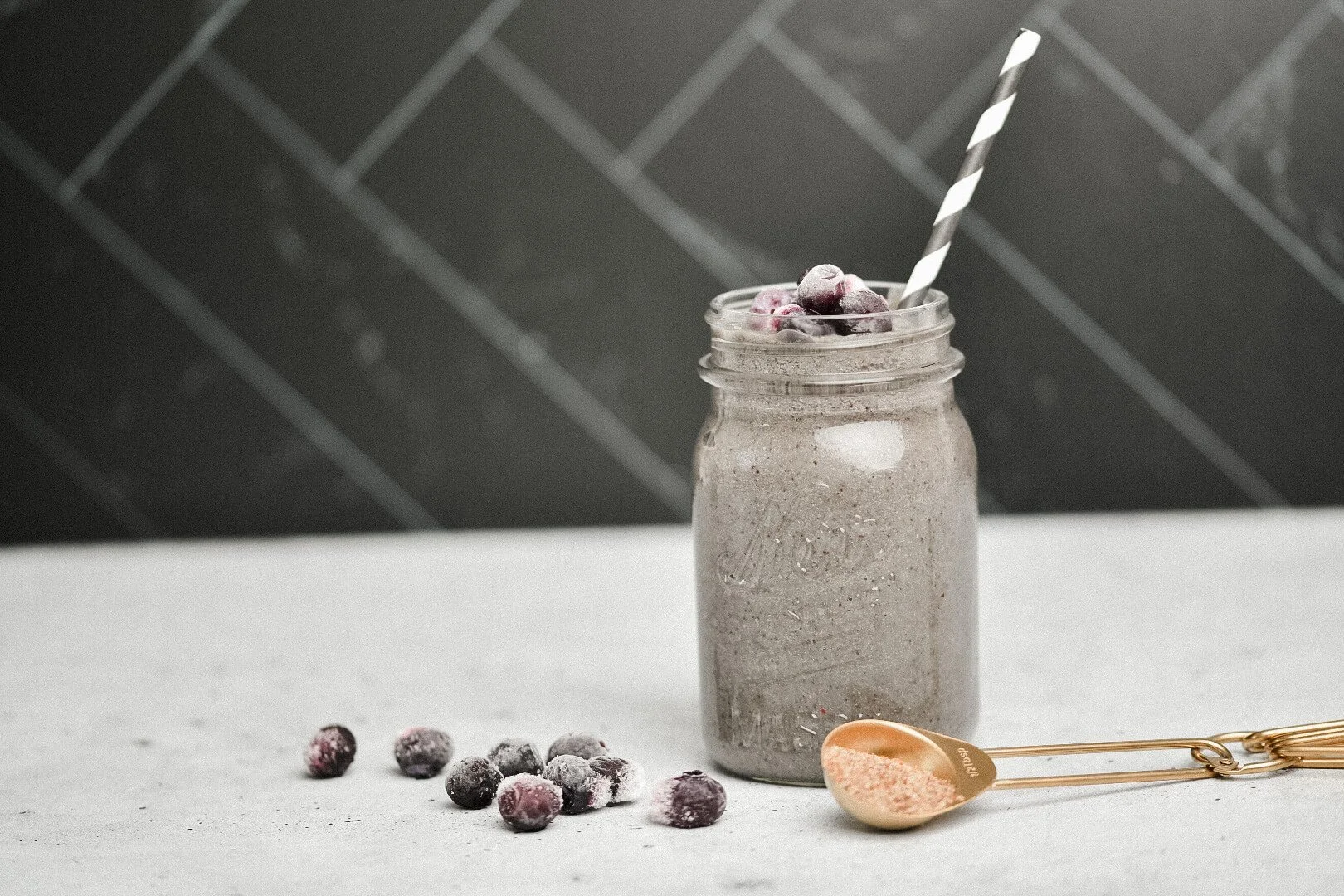 A superfood smoothie in a mason jar, made with a superfood mix and topped with frozen blueberries.