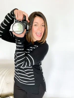 A portrait of a smiling woman holding a camera, representing a professional photographer available for hire.