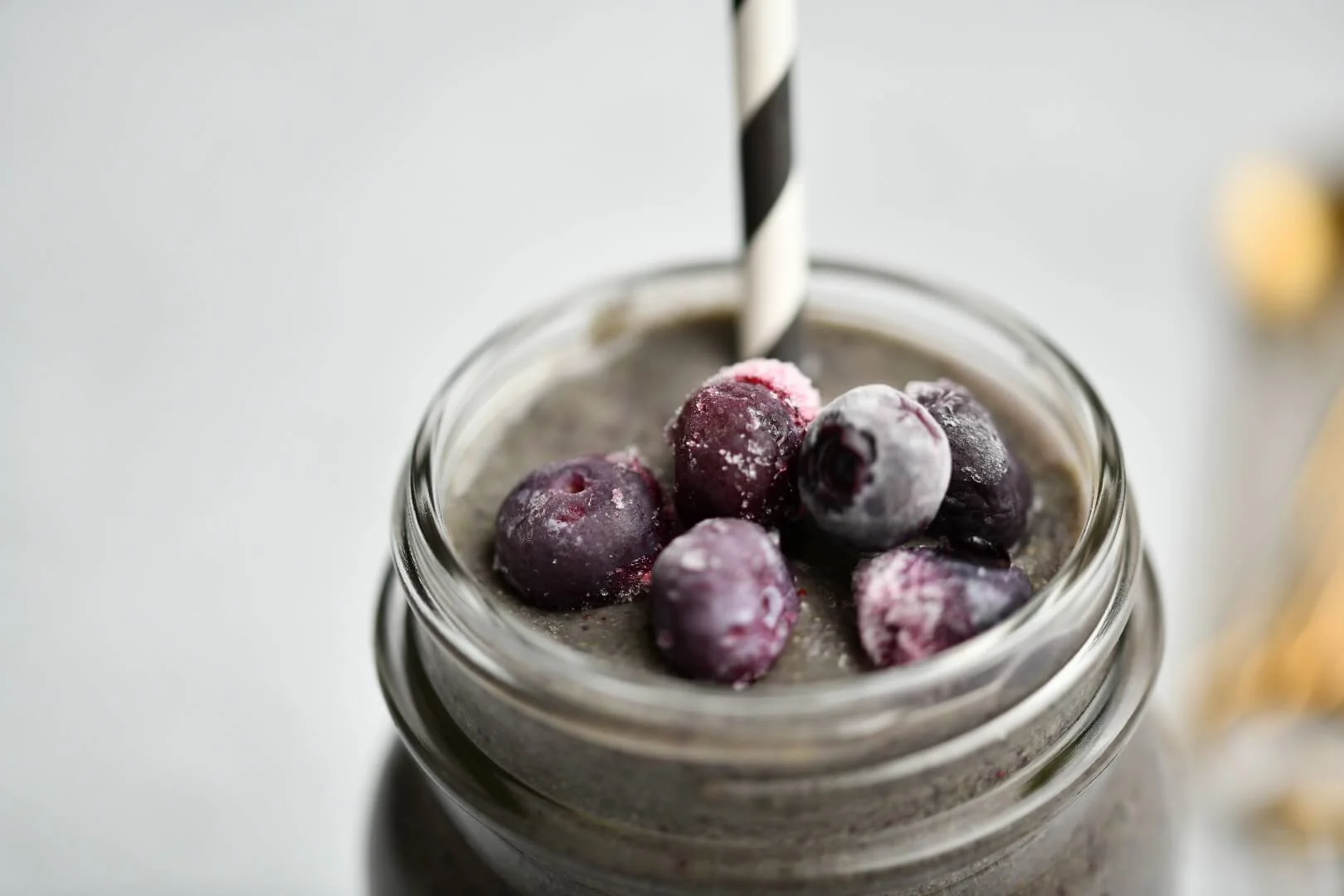 A superfood smoothie made with a mix of ingredients, topped with frozen blueberries and a striped straw.