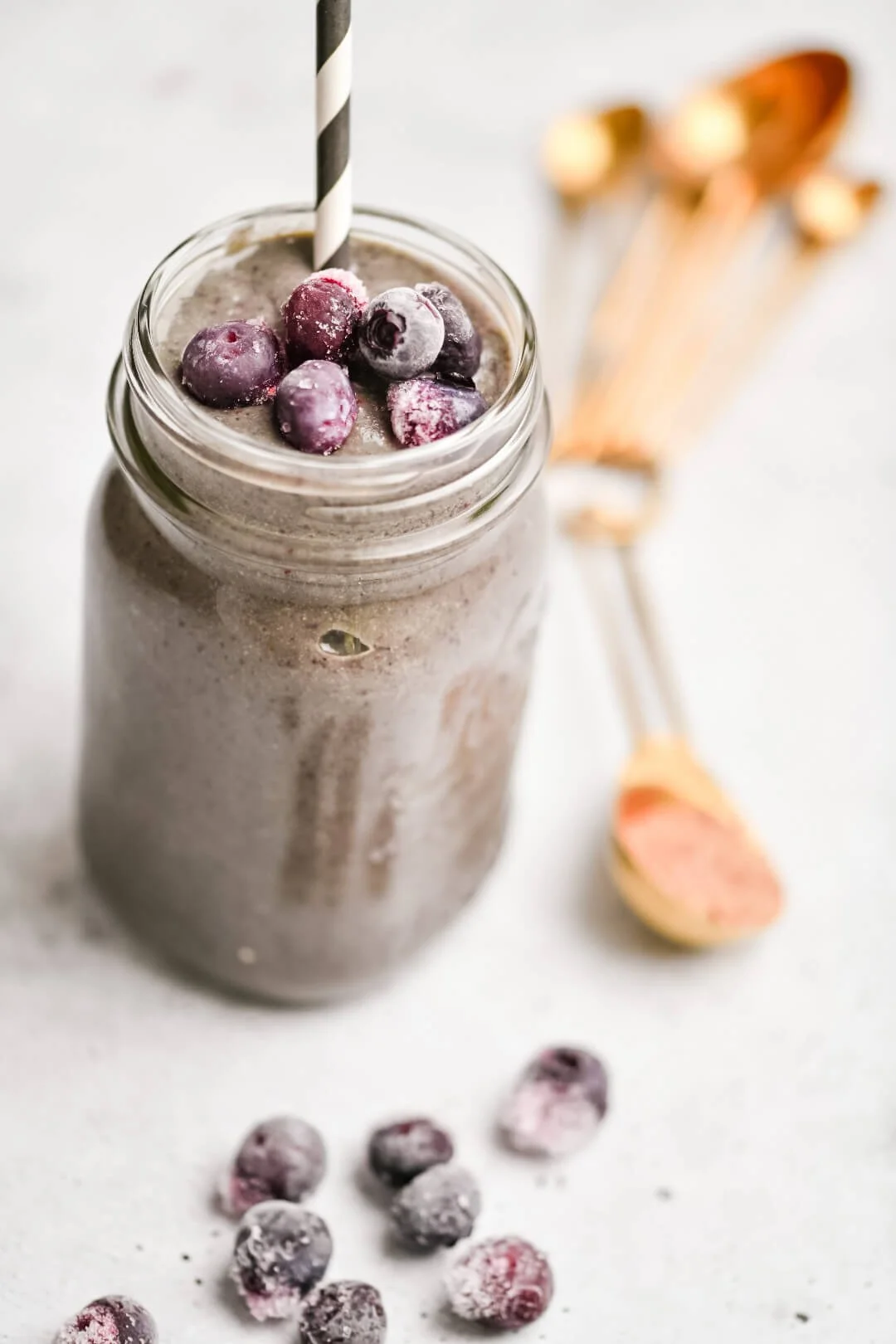 A superfood smoothie in a mason jar with a striped straw and frozen blueberries, representing a superfood smoothie recipe.