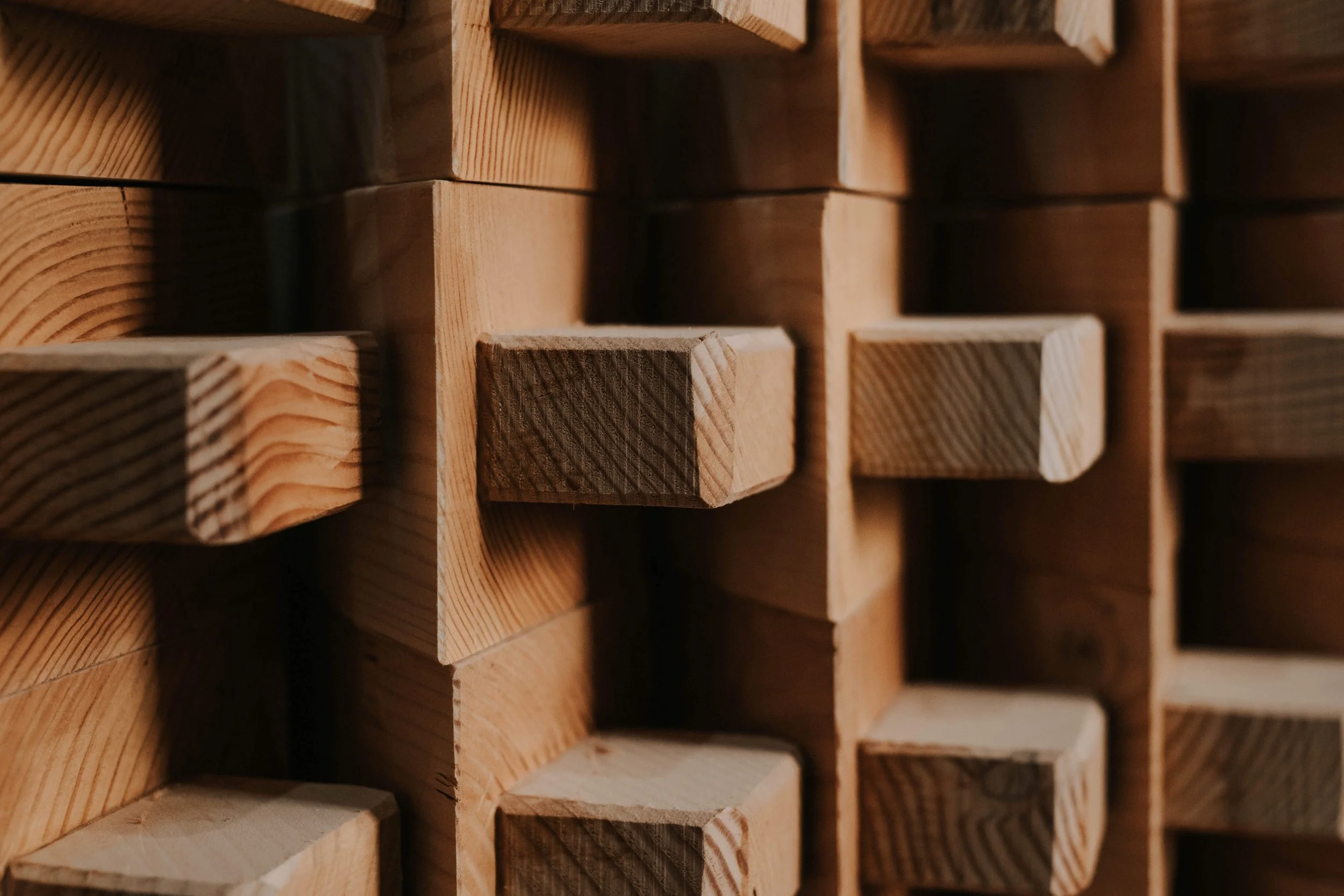 A close-up of a wall with a three-dimensional geometric pattern made of wooden blocks, highlighting the texture and natural wood grain.