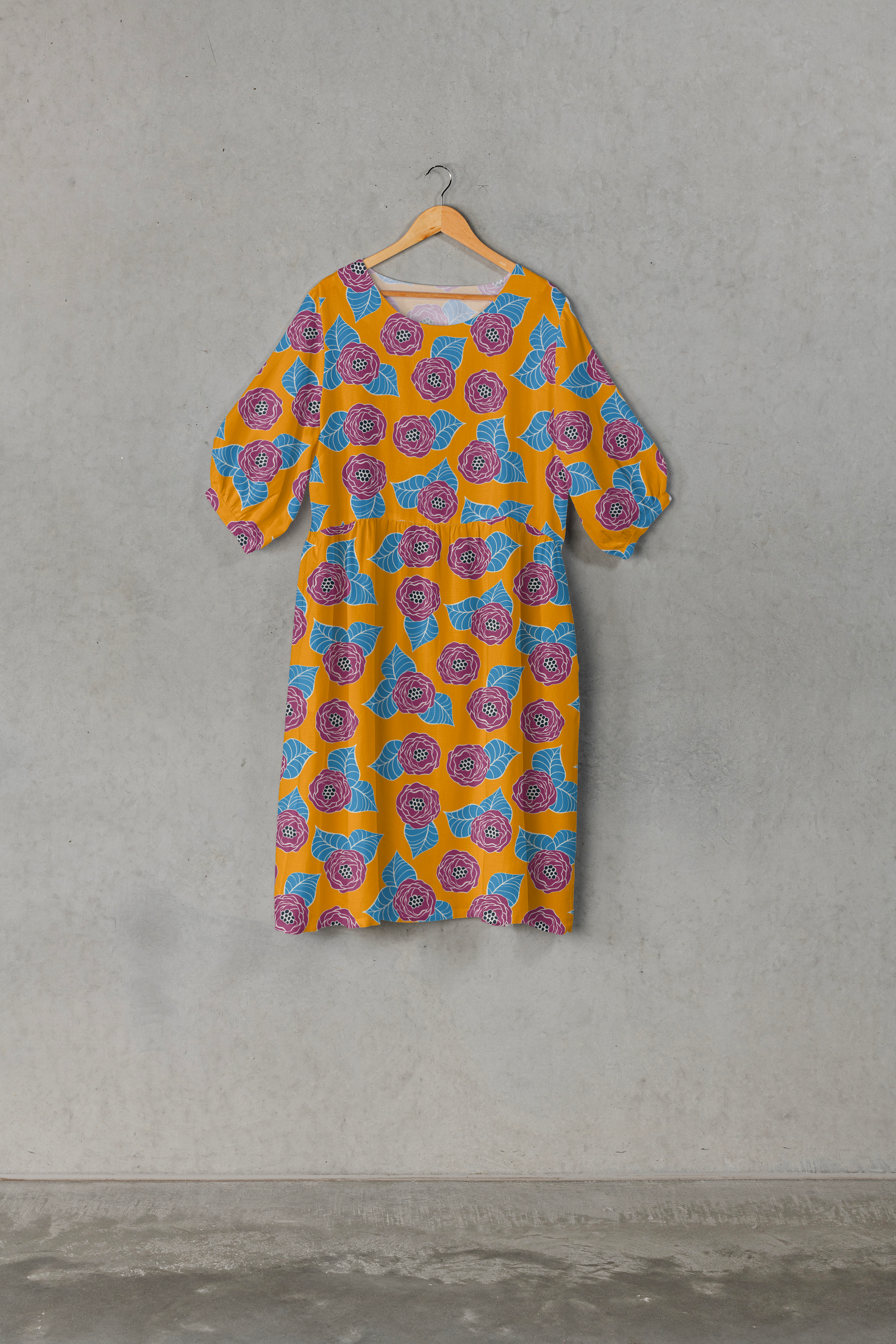 A dress with a yellow background and a pattern of purple roses with blue leaves hanging on a wooden hanger against a plain gray wall.