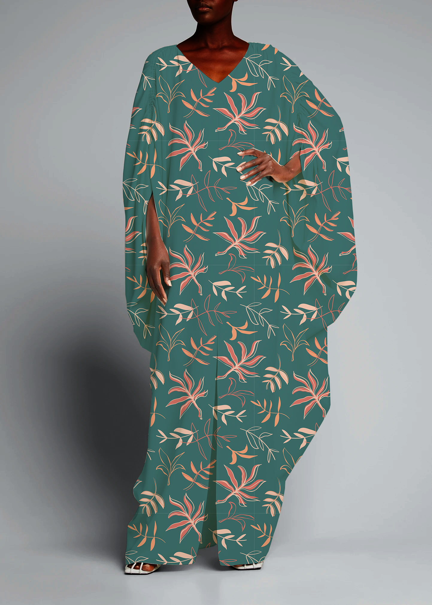 A woman wearing a teal dress with a pink and beige floral pattern, standing against a plain gray background.