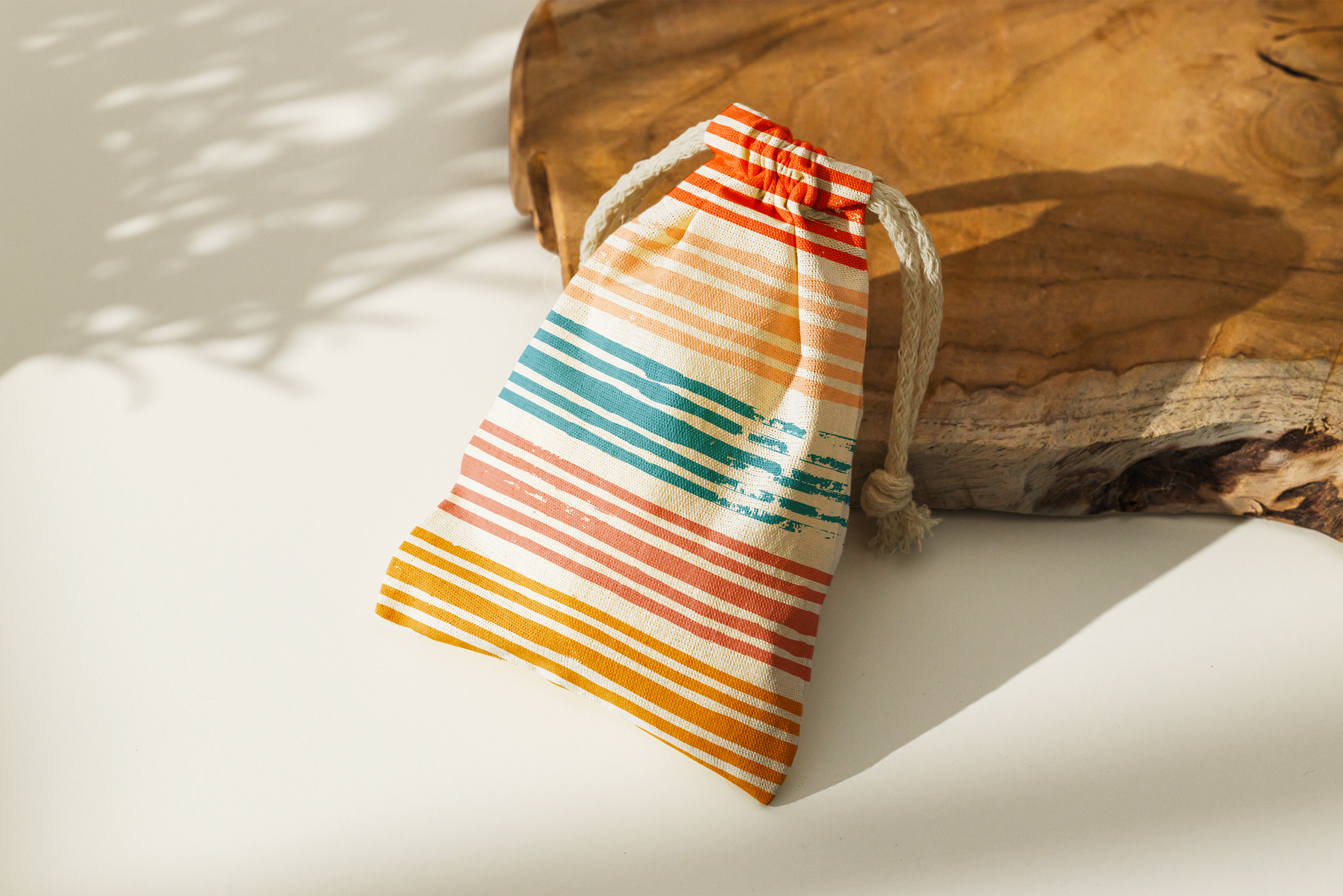 Colorful, striped paper gift bag with white rope handle, placed on a white surface against a piece of driftwood.