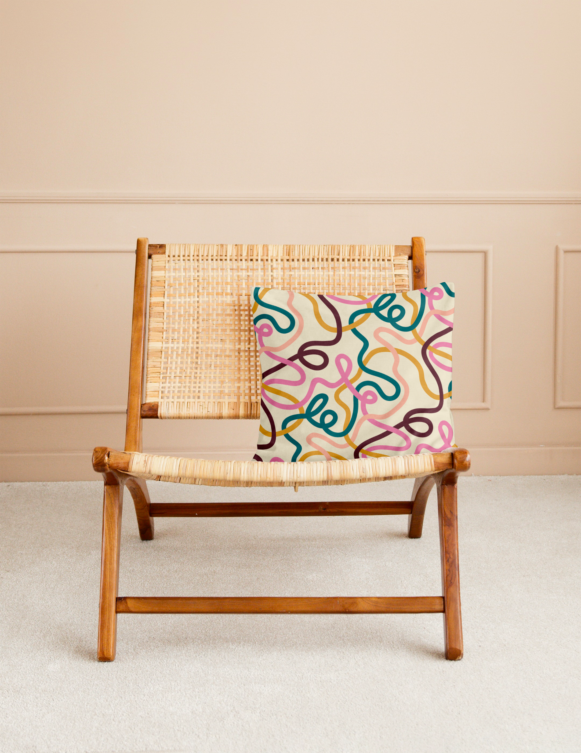 A wooden chair with woven seat and backrest, a colorful abstract-patterned pillow draped over the back, set against a beige wall with decorative molding.