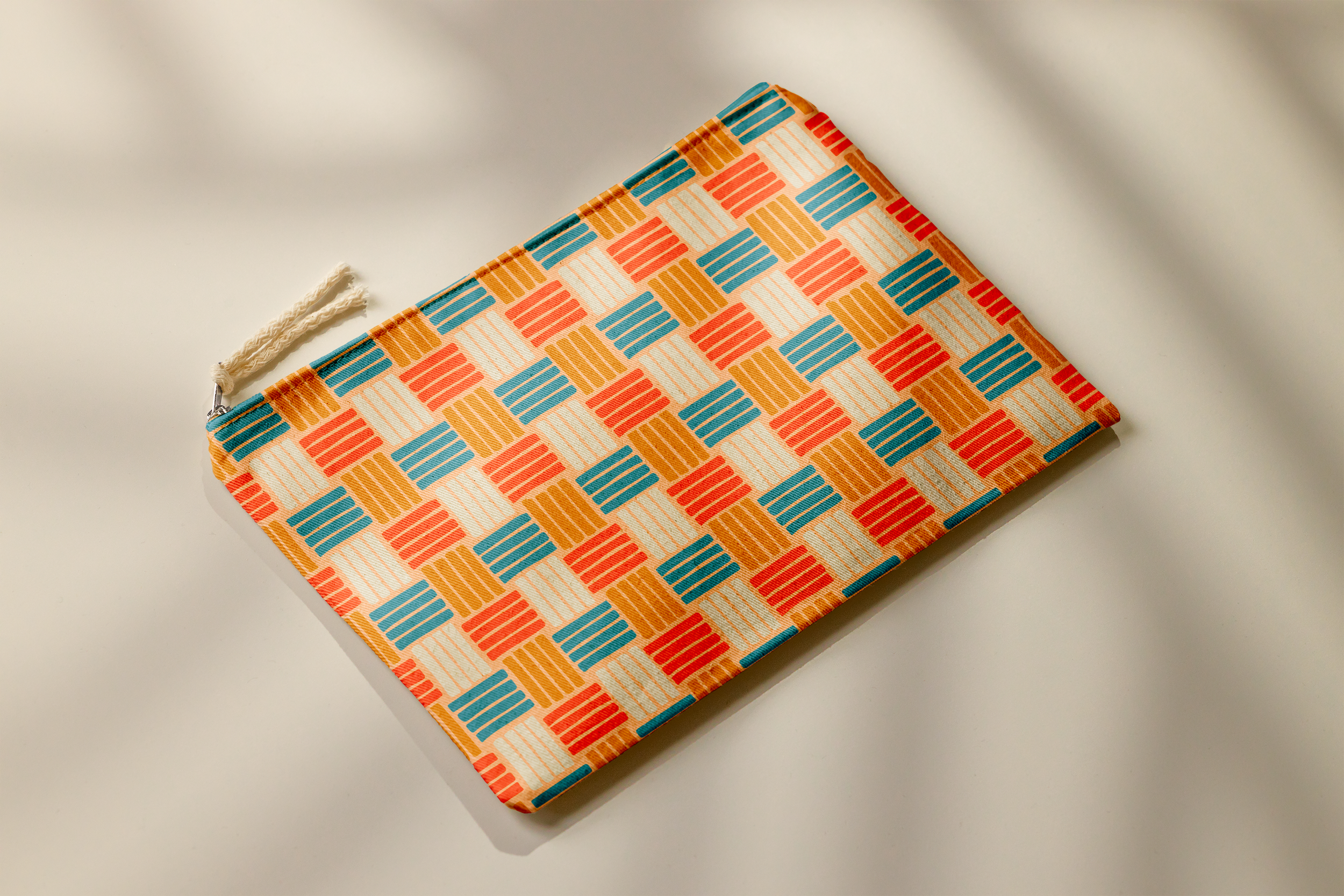 A colorful fabric pouch with a geometric pattern in shades of orange, blue, red, and cream, lying on a white surface.