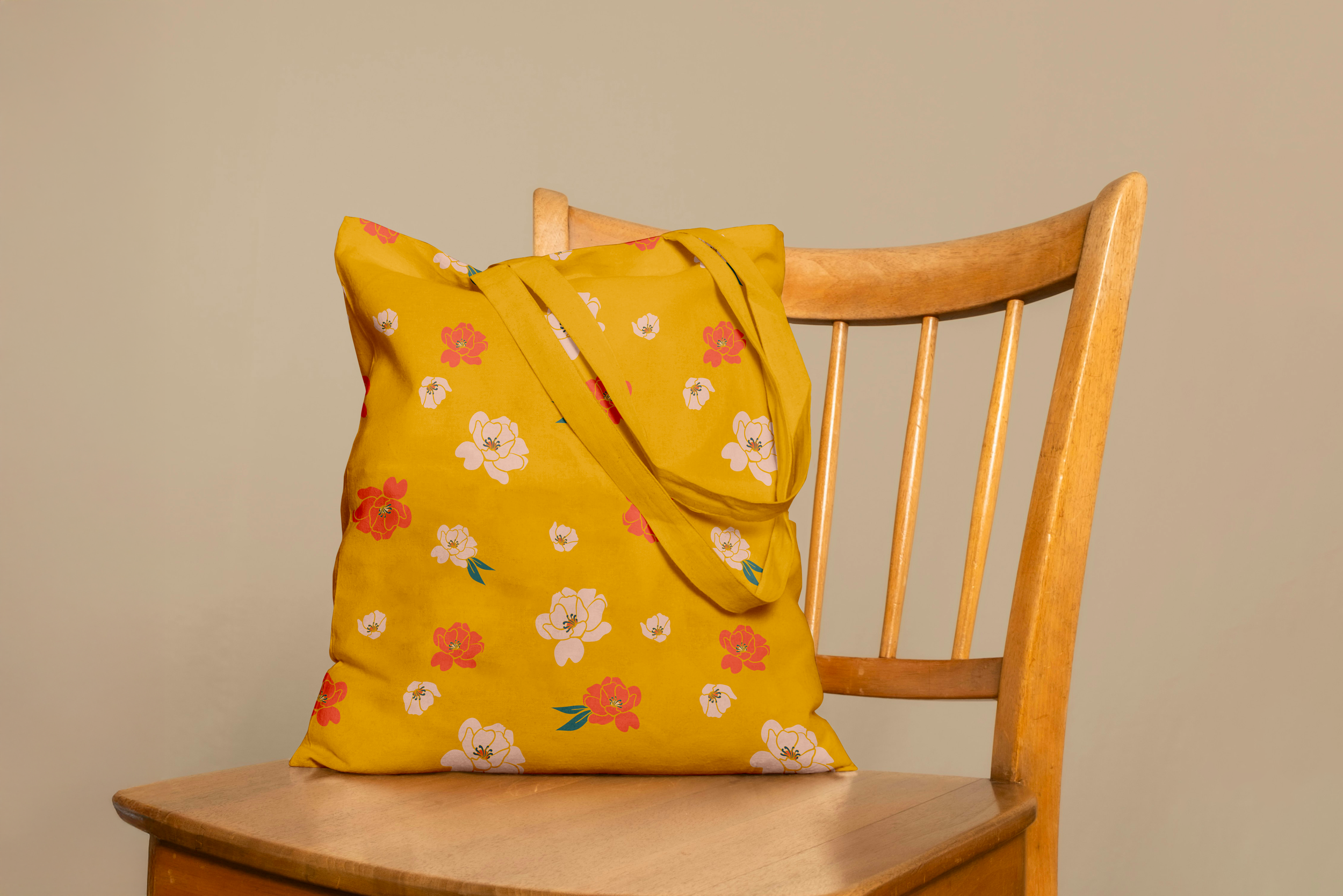 A yellow tote bag with a floral pattern rests on a wooden chair with a light beige background.