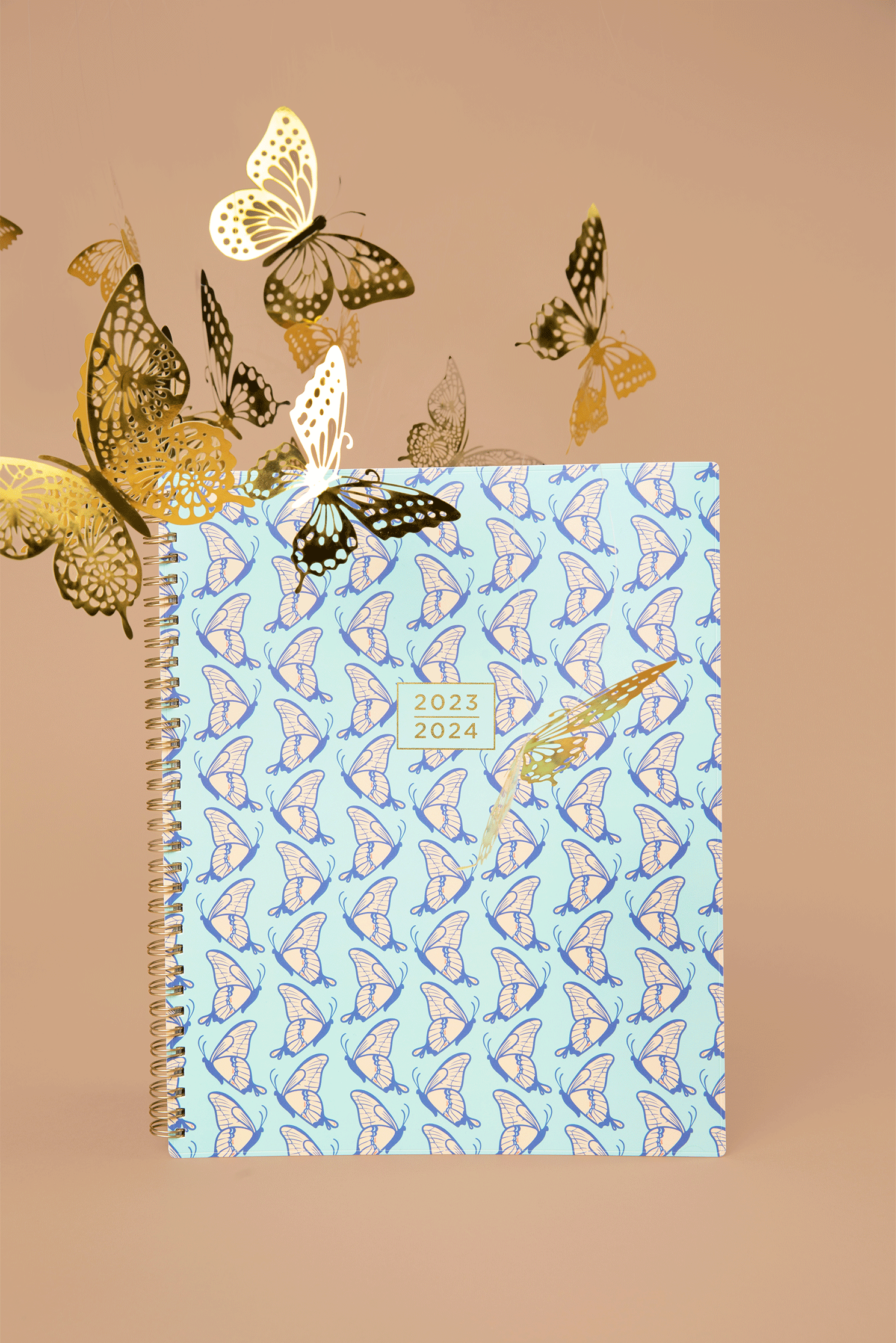 A planner with butterfly patterns on the cover, featuring the years 2023 and 2024, surrounded by gold butterfly paper cutouts on a brown background.