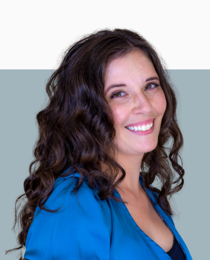 Rachael Black with long, curly brown hair, smiling, wearing a blue shirt, standing against a background split horizontally between white and gray.