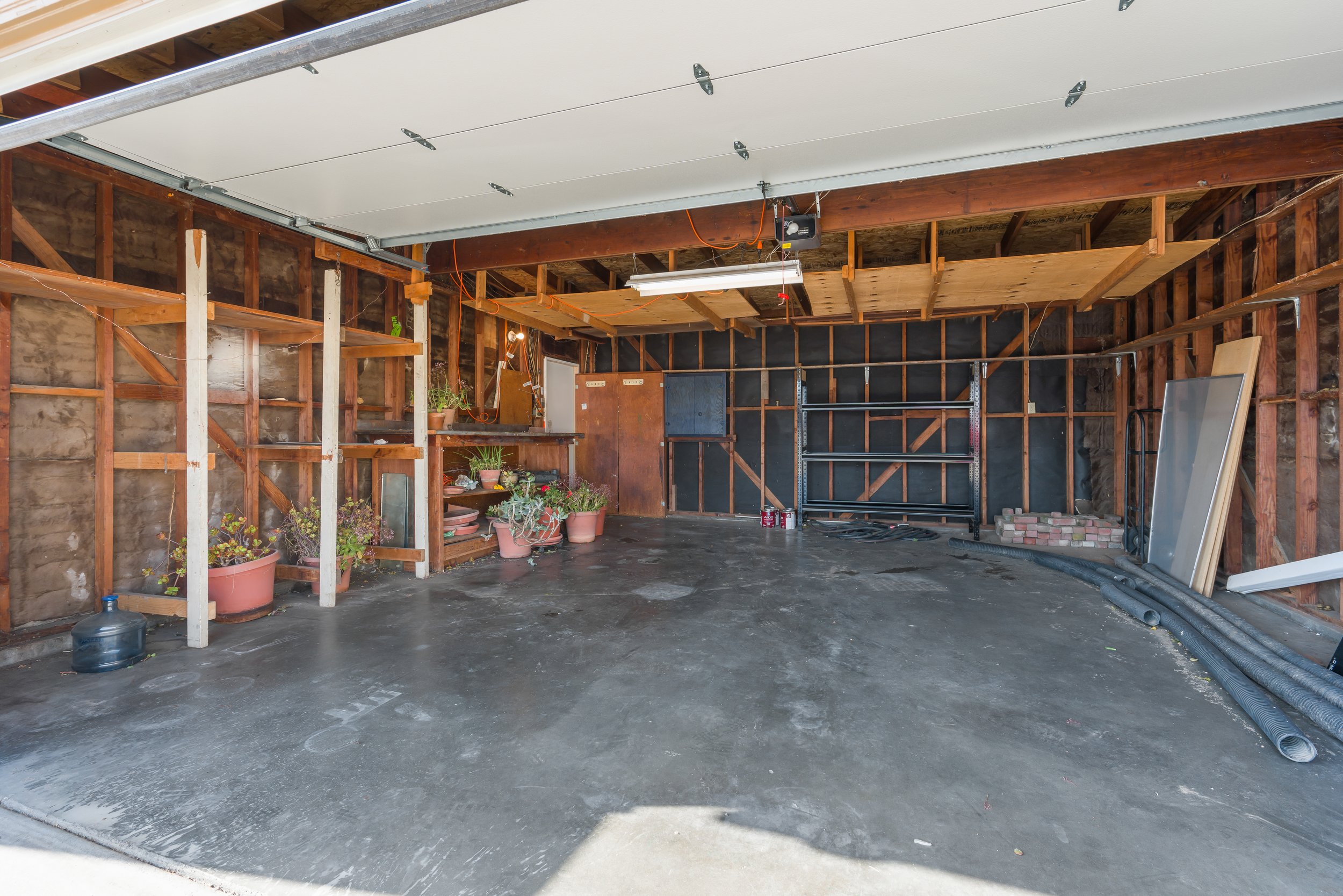 Spacious garage with exposed framing, concrete flooring, built-in shelving, and ample storage space. Ideal for parking, workshop use, or future improvement opportunities in this Santa Cruz County residence.
