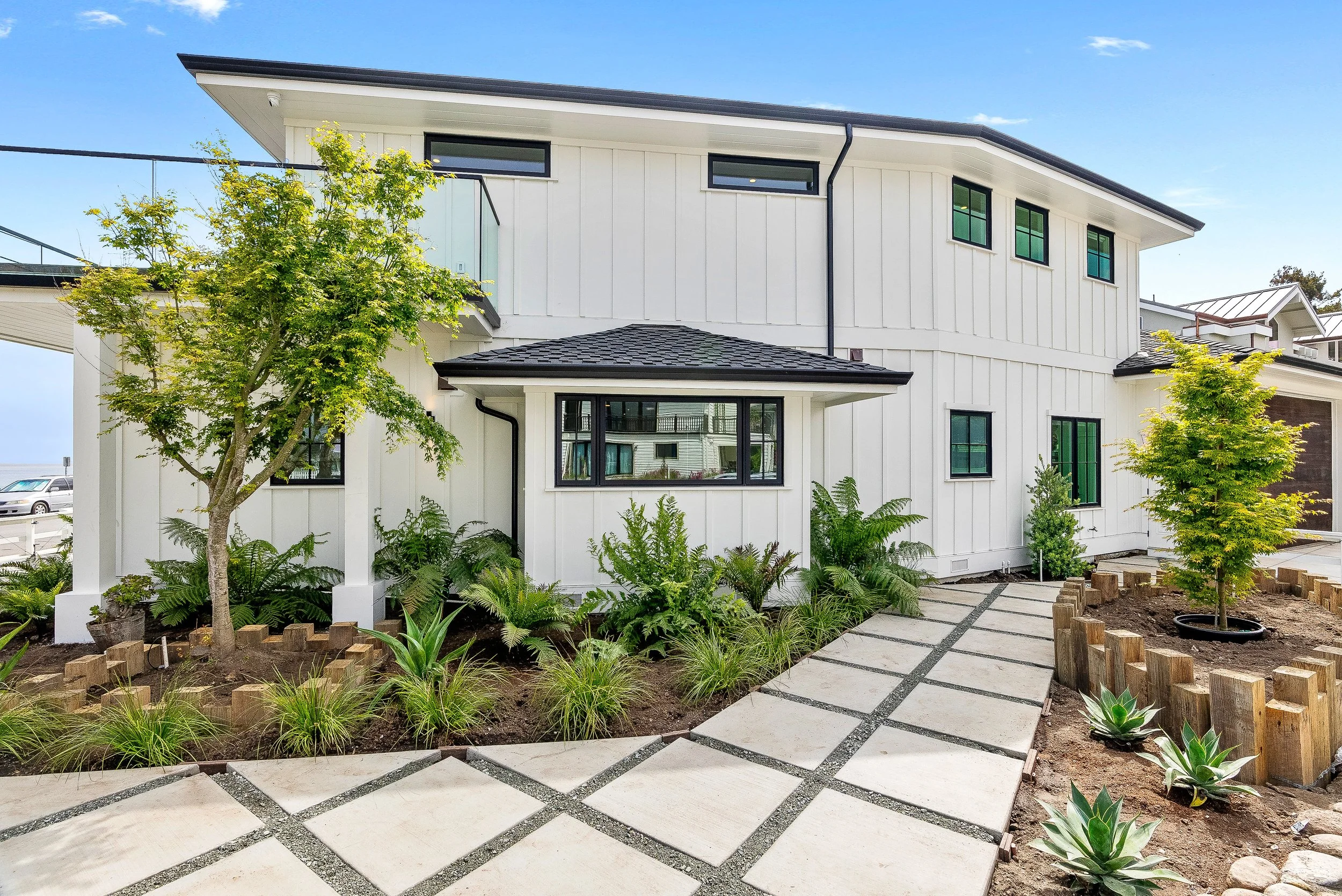 Modern white house with landscaped front yard, small trees, and a concrete walkway in Capitola, California.