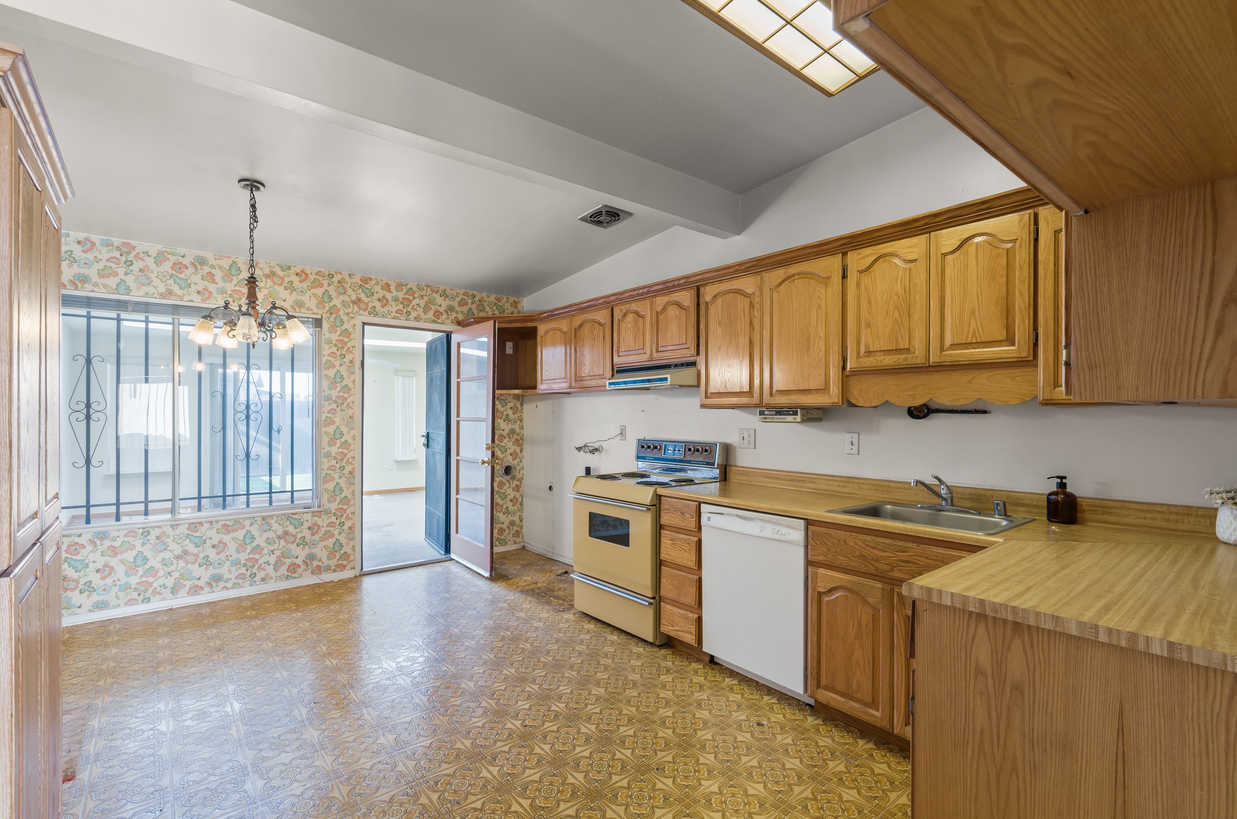 Kitchen with wooden cabinets, yellow stove, dishwasher, and sink, with a window and chandelier, and floral wallpaper in Salinas, Monterey county, CA.