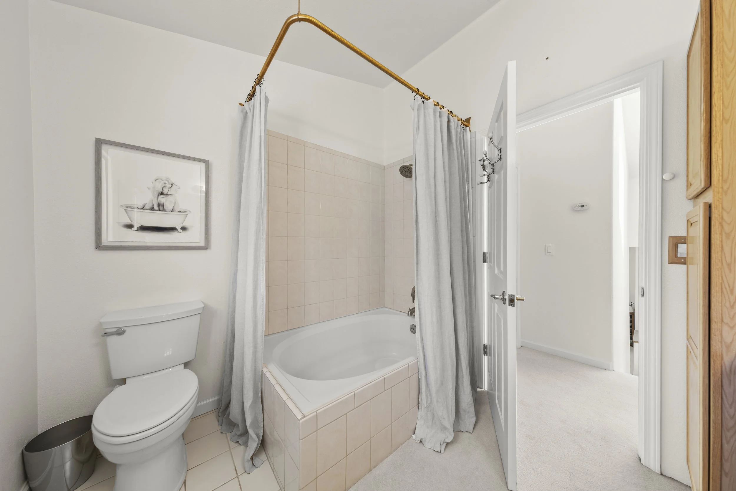 Bathroom with white walls, a toilet, a bathtub with pink tiles and a gray curtain, and a framed picture of a dog in a bathtub on the wall.