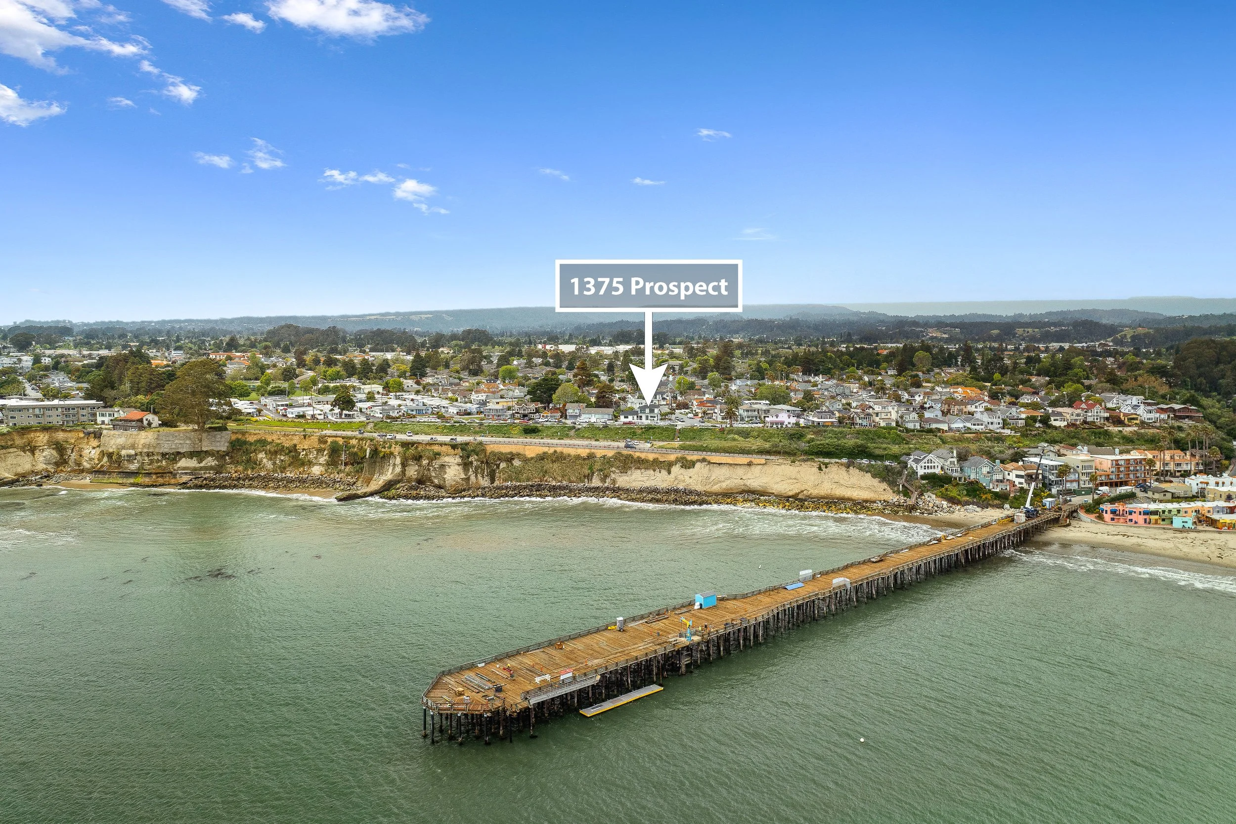 Aerial view of a coastal town with a pier extending into the water, with a residential area on cliffs in the background and a label pointing to '1375 Prospect' in Capitola.