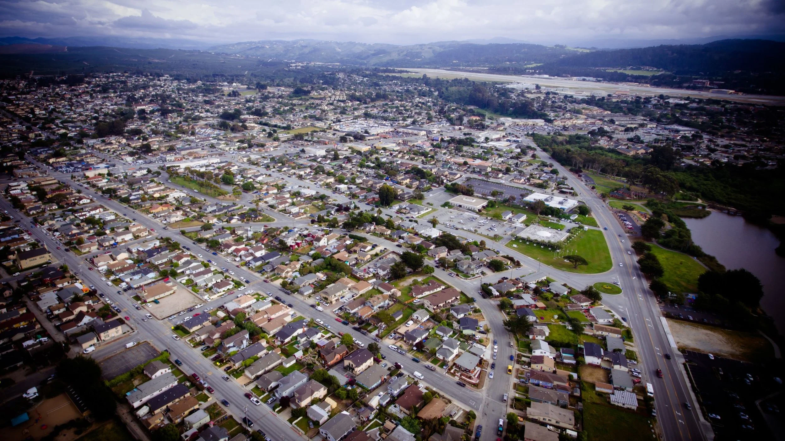 Aerial view of a suburban neighborhood with a mix of houses, streets, a park, and a body of water surrounded by trees Salinas Area.