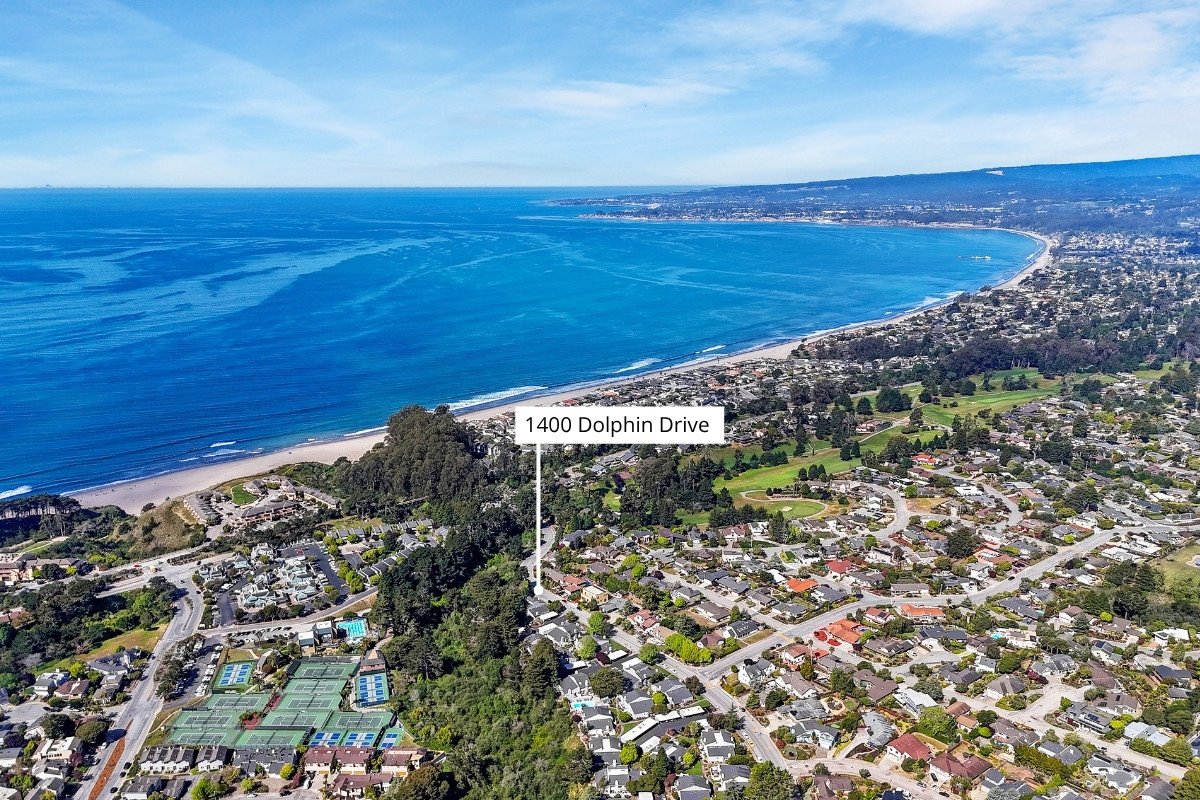 Aerial view of a coastal residential area with tennis courts, houses, and a beach, near the ocean.