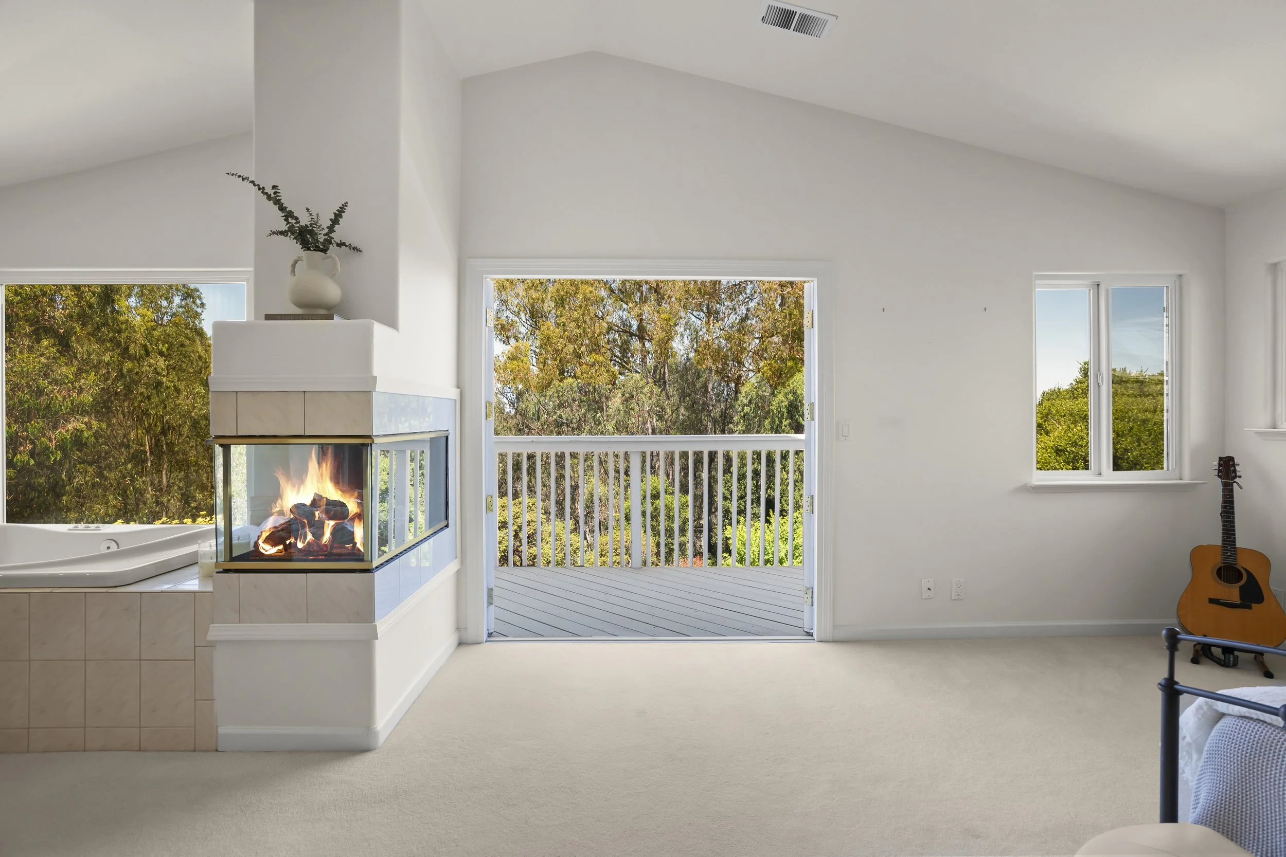 Living room with a fireplace, sliding door opening to a balcony with view of trees, guitar, and window