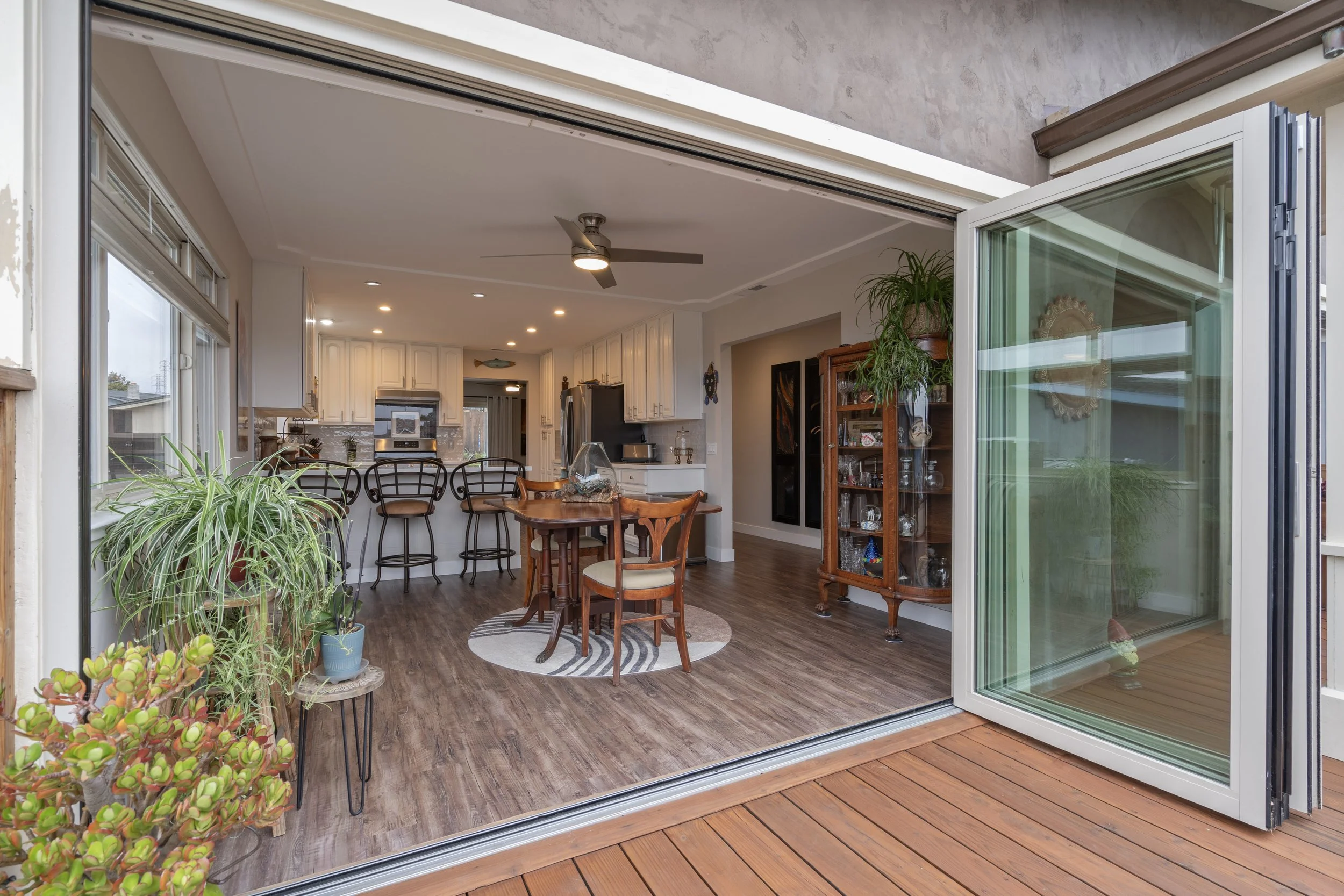 Open sliding glass door leading into a kitchen and dining area with wooden furniture, potted plants, and hardwood flooring.