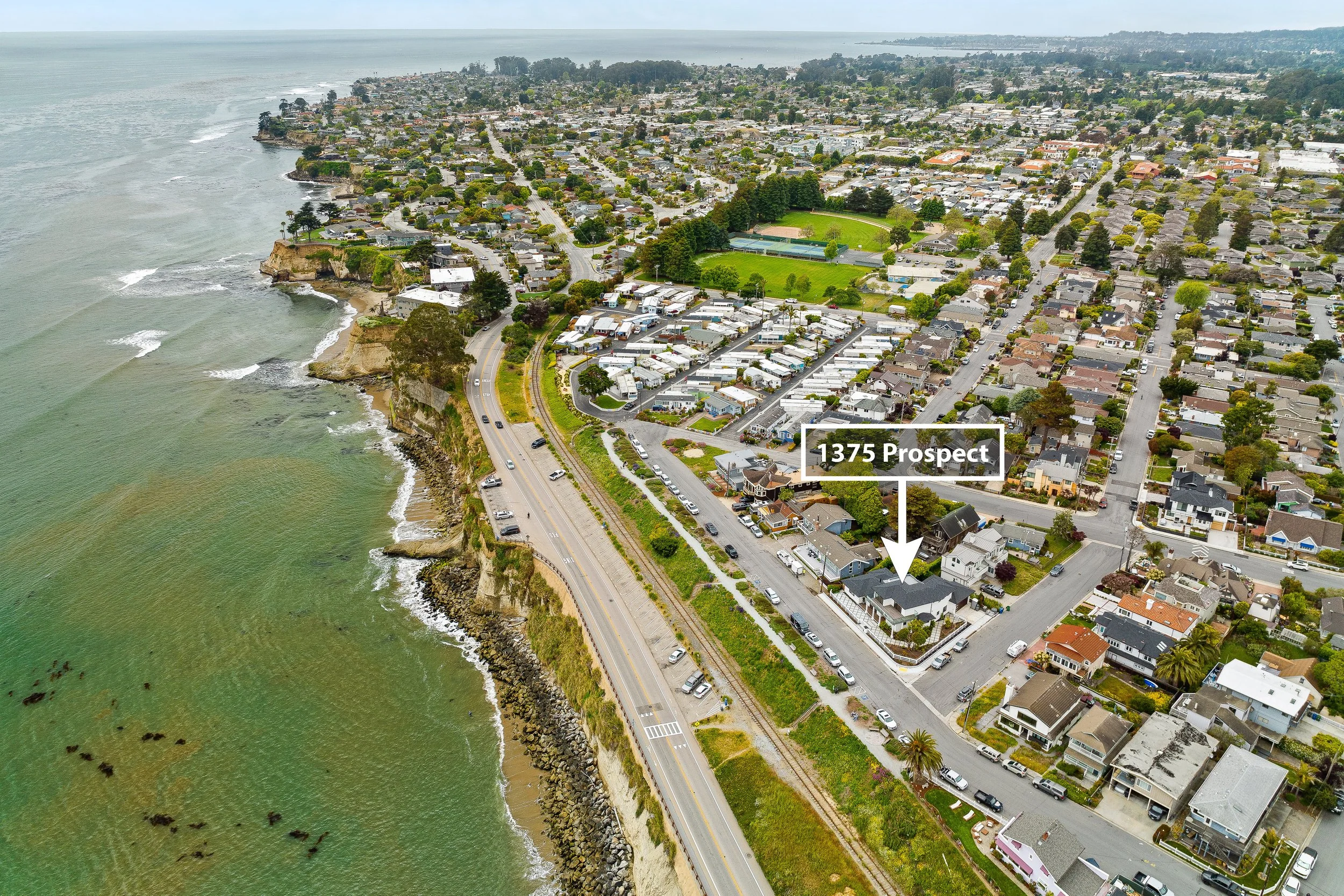 Aerial view of a coastal neighborhood with houses, a park, and streets along the shoreline, with the ocean on the left side and a label pointing to 1375 Prospect.\ in Capitola, California.
